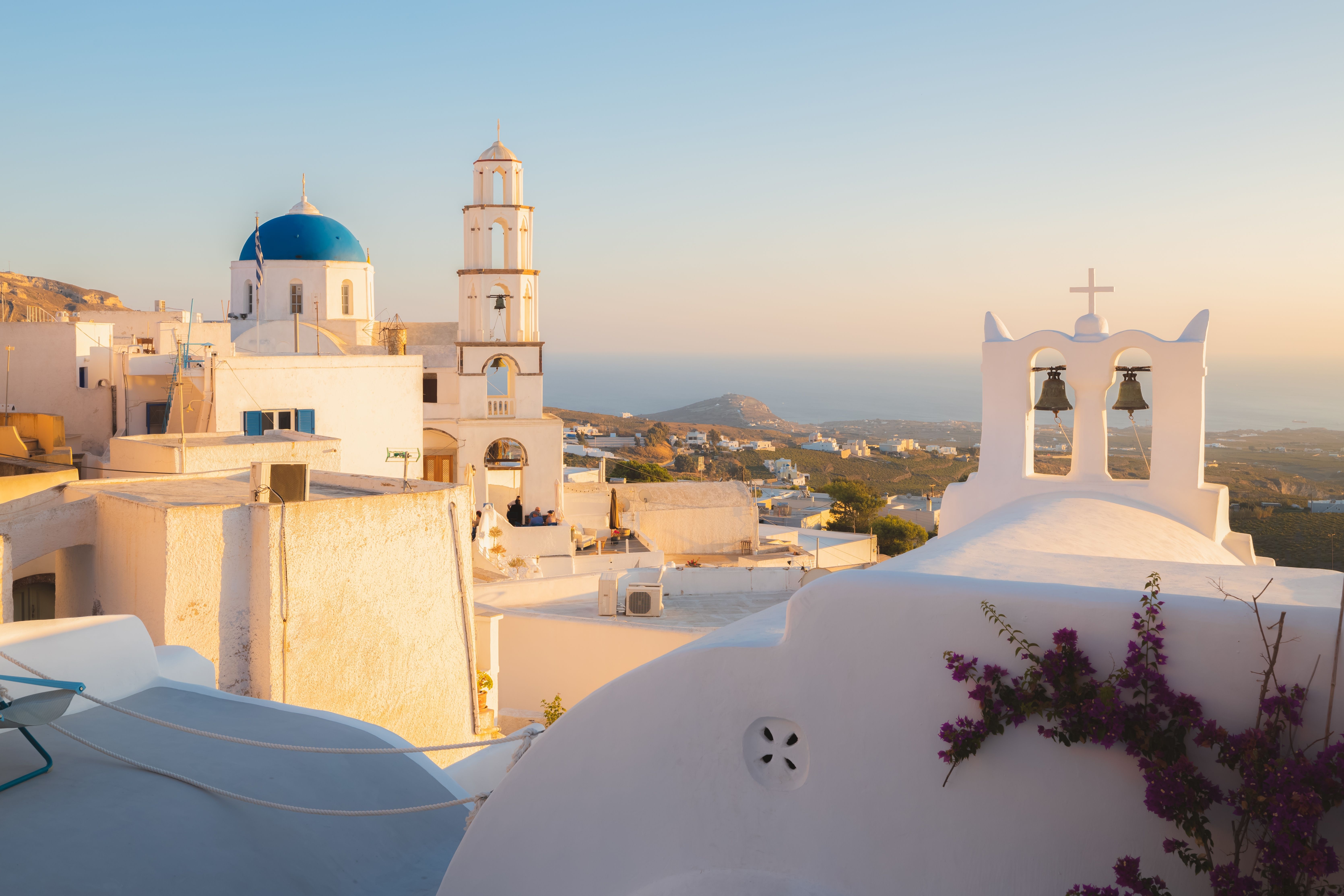 Sunset views over a whitewashed, blue-domed church; church bells and a tall tower in Santorini