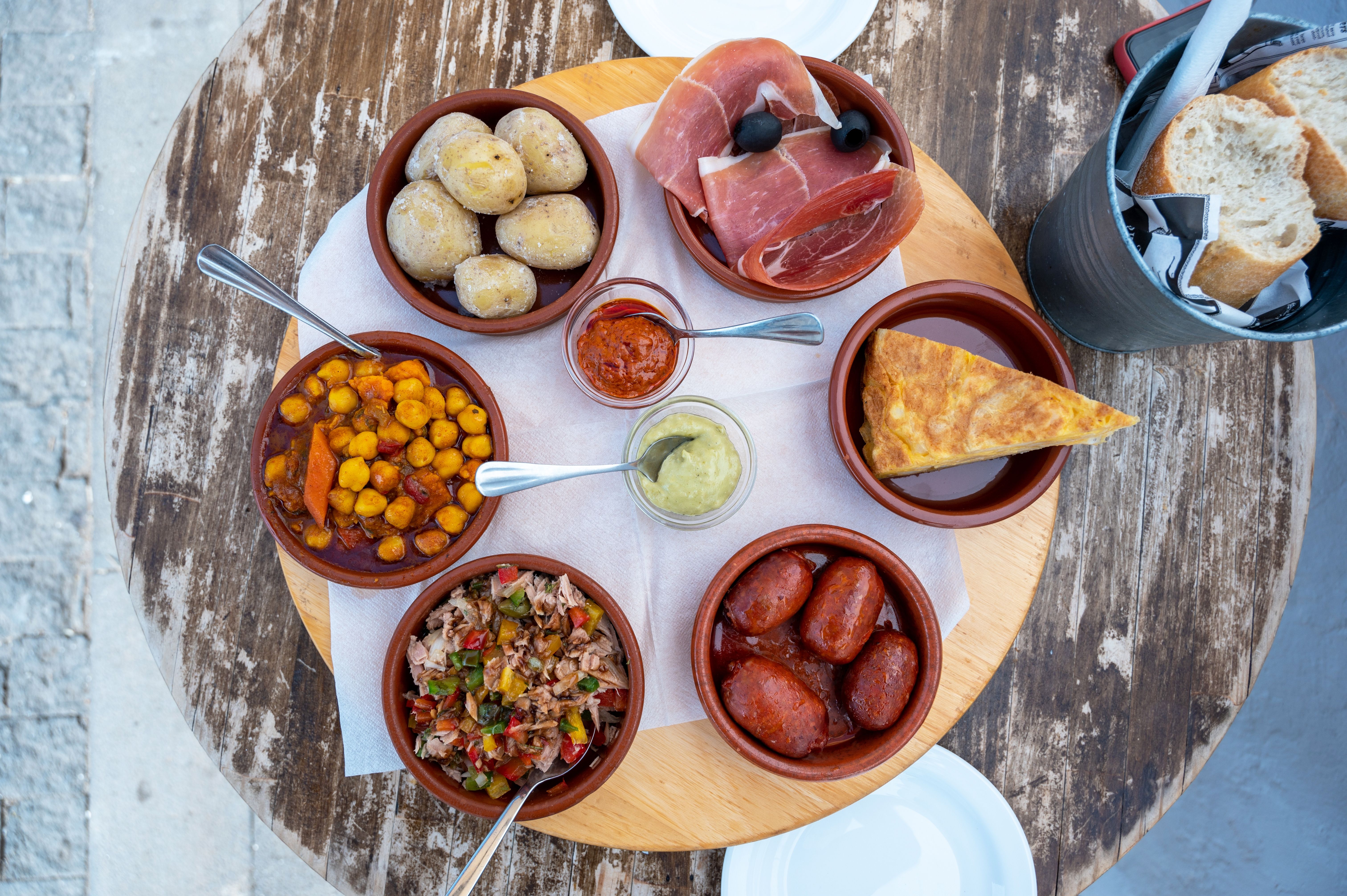 A bird's-eye-view image of six tapas dishes on an outdoor cafe table