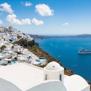 A view of the white houses on Santorini in the Cyclades, Greece on a clear sunny day with the sea in view and a cruise ship in sight