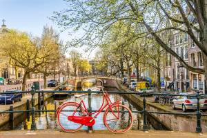 A red bike parked on a bridge that crosses a canal in Amsterdam