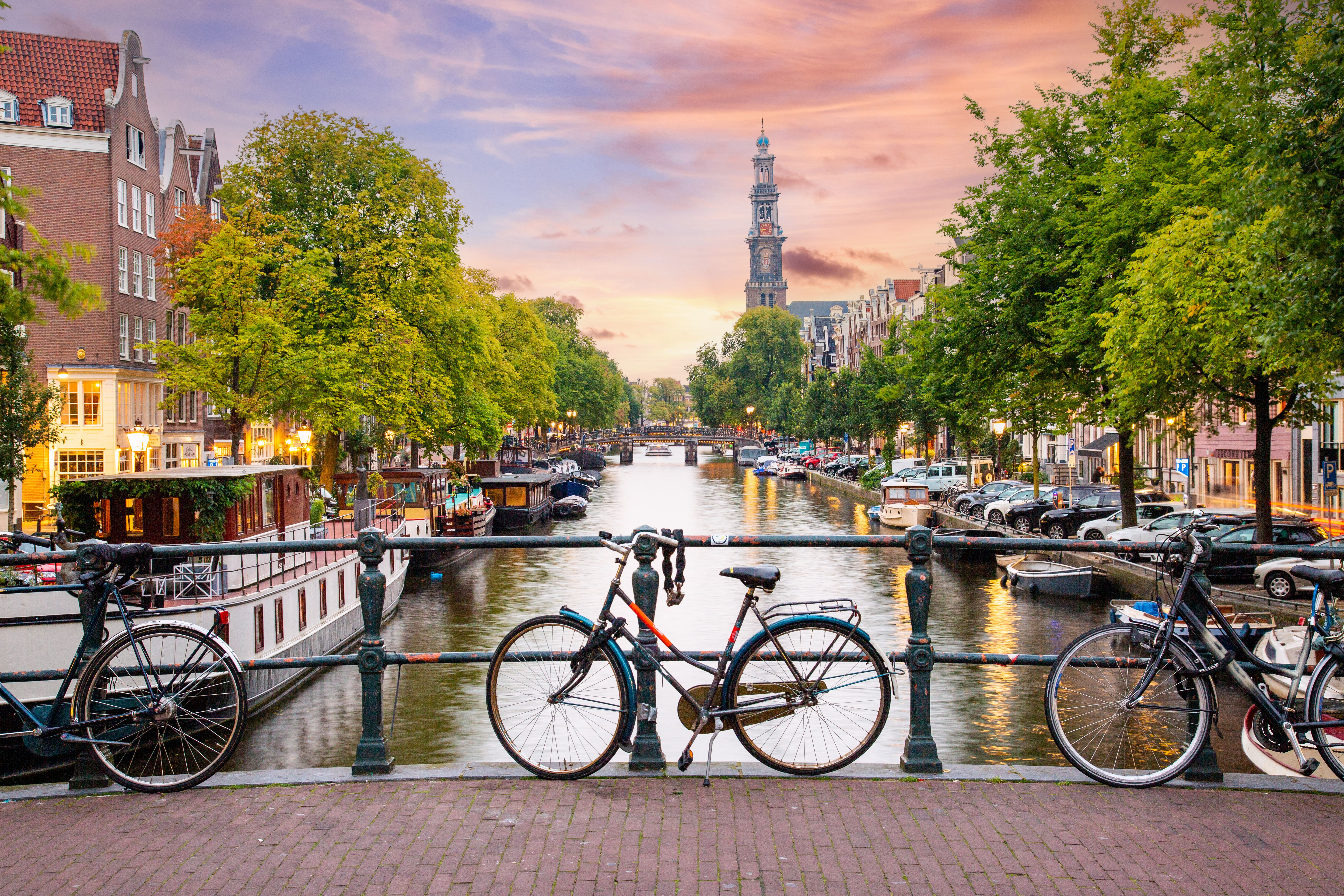 Sunset in Amsterdam with Bicycles parked on a bridge over a canal in the city centre, with typical Dutch houses on the background and streets illuminated with lights