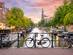 Sunset in Amsterdam with Bicycles parked on a bridge over a canal in the city centre, with typical Dutch houses on the background and streets illuminated with lights