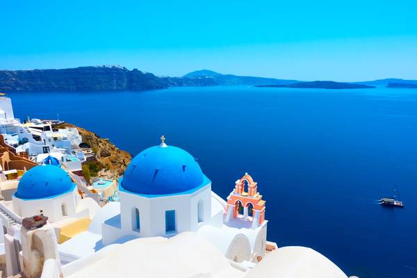 A panoramic view from Oia town on the island of Santorini with a Greek orthodox church with the iconic blue domes and sea