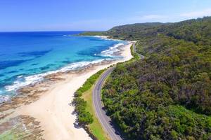 Aerial view of a winding road that hugs the south coast of Australia with bush on the right side and a golden beach to the left
