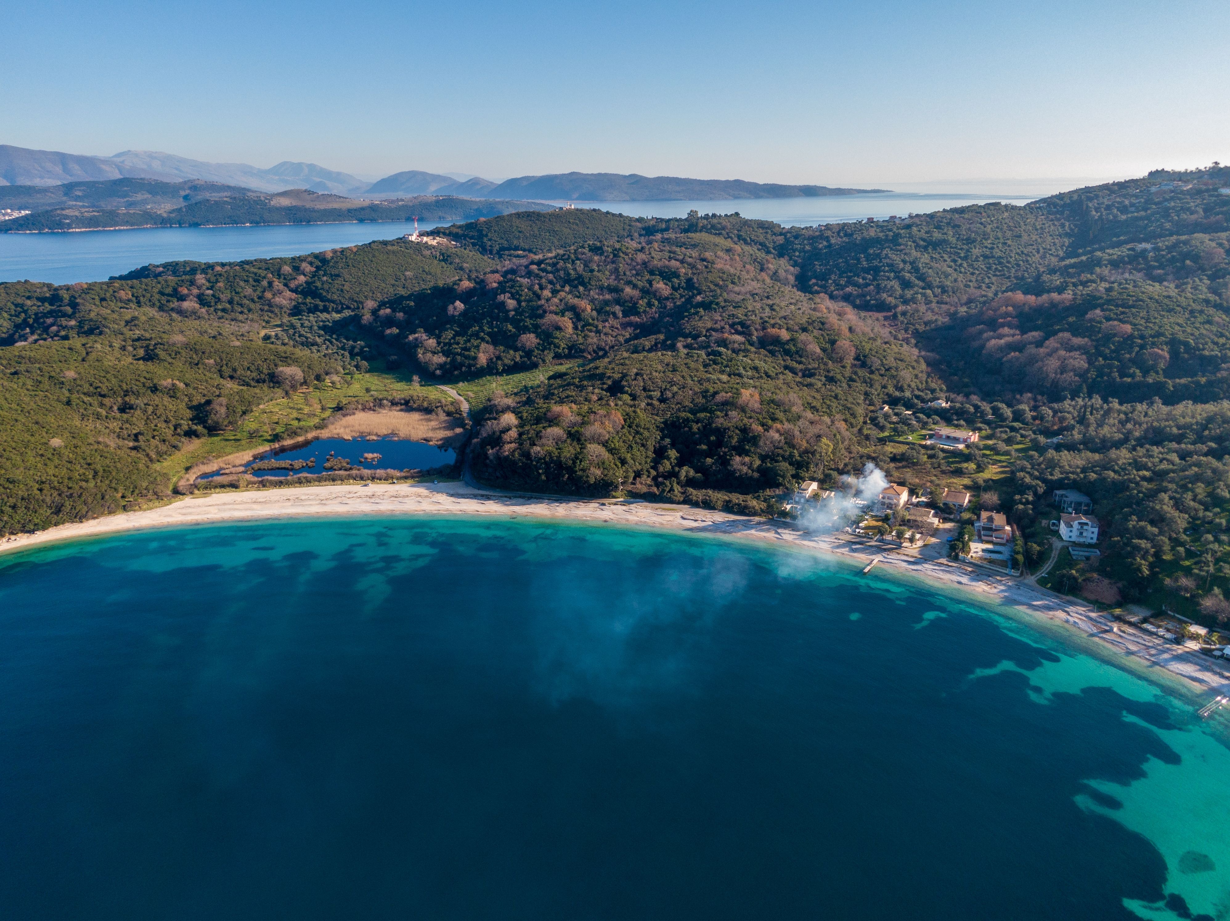 Aerial drone view of a sandy curved beach with crystal-clear waters in Corfu, Greece