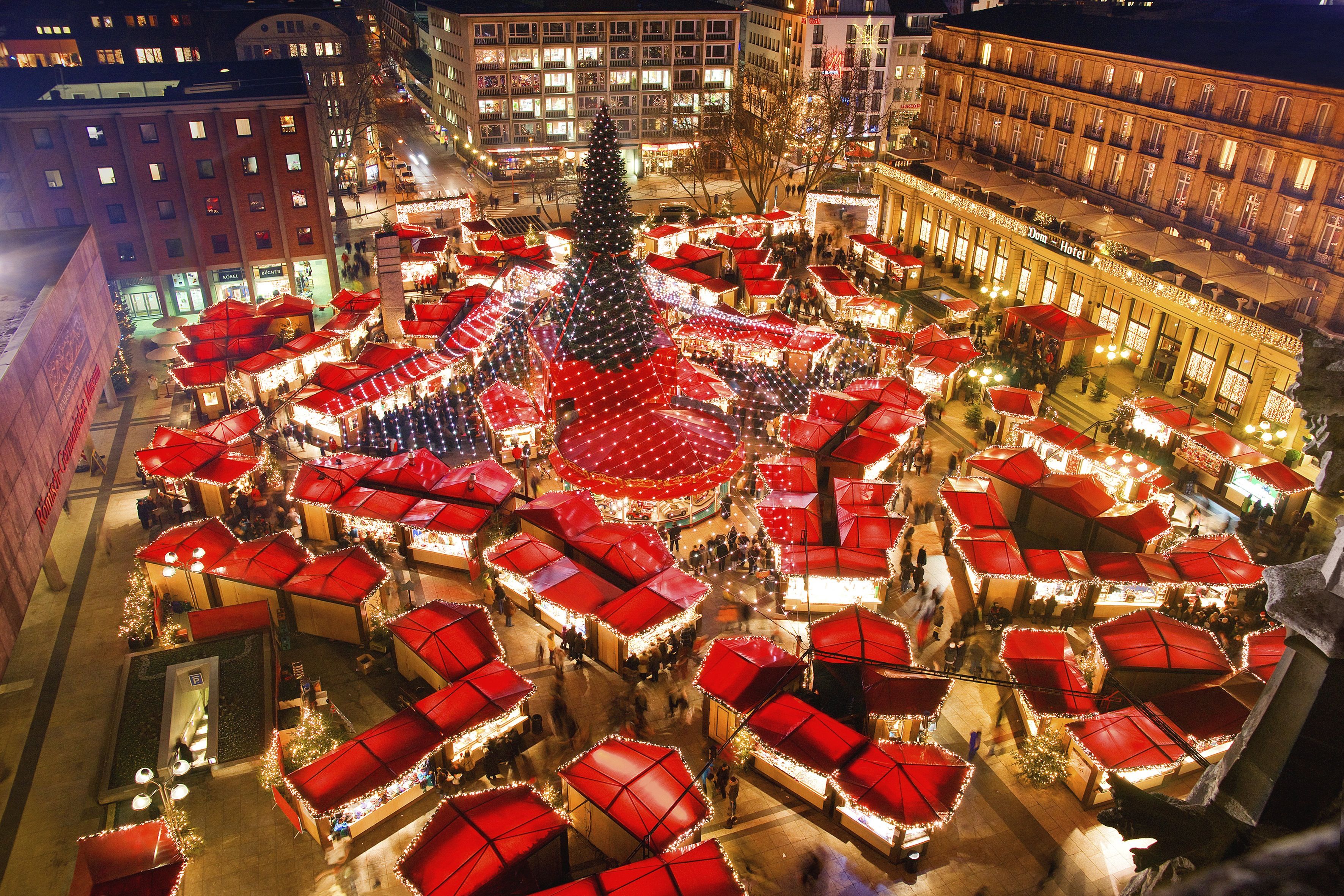 An aerial view of Cologne Christmas market with red-roofed market stalls and a central Christmas tree