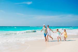Parents and two children holding hands walking happily along a tropical beach