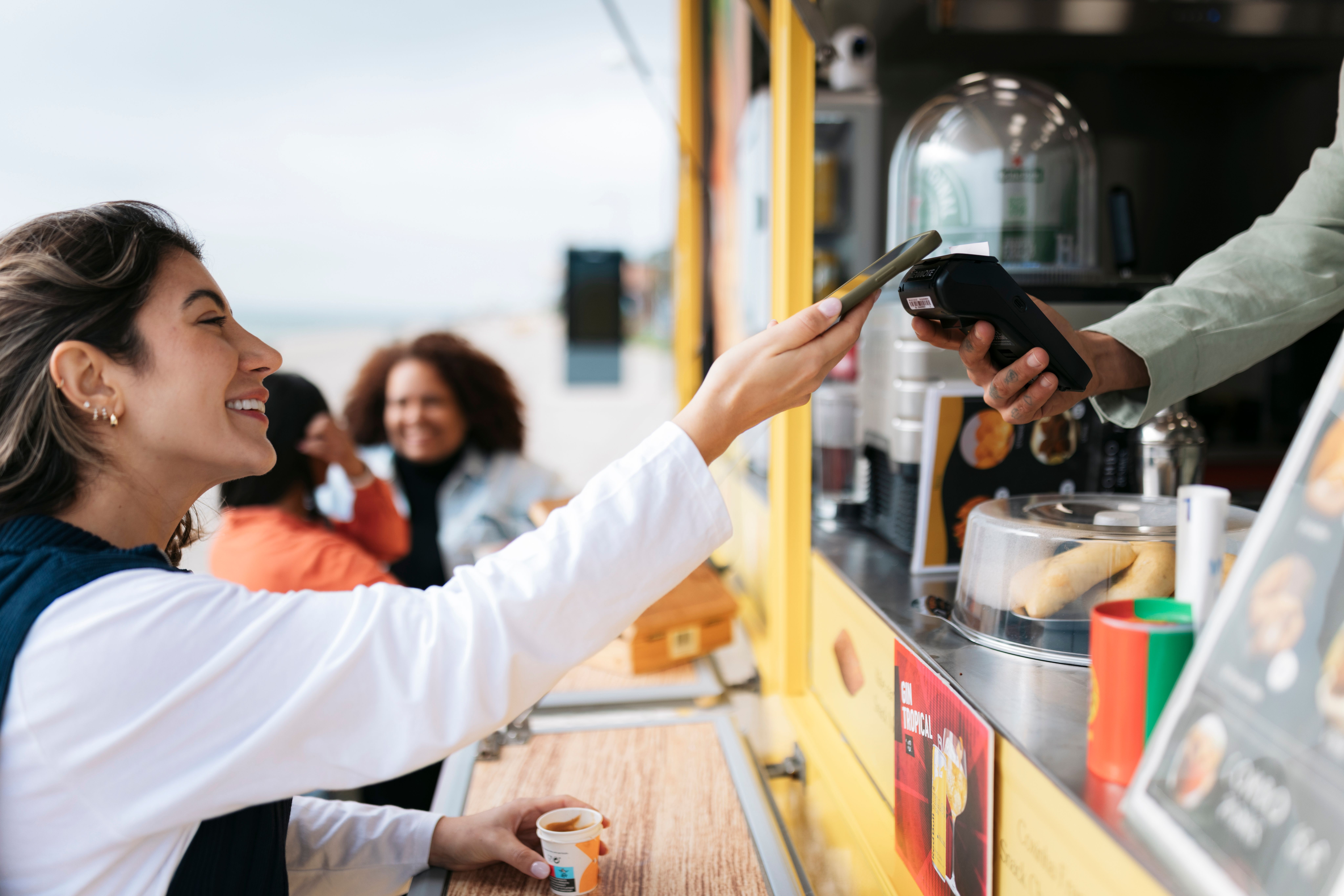 Cheerful young woman paying with a smartphone at a food truck by the beach