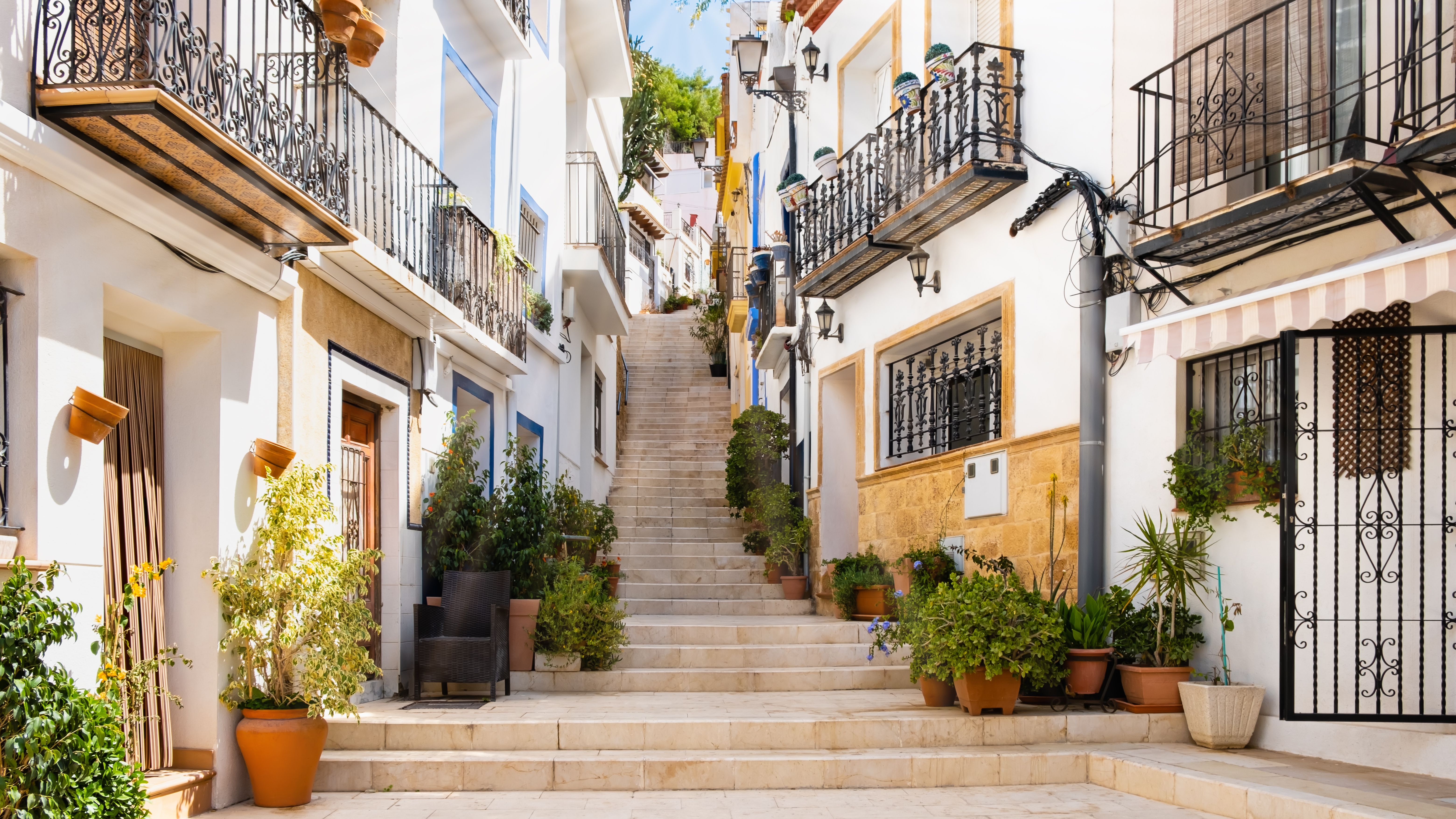 A view of a stepped back street in Alicante old town, lined wither side with white houses with black metal balconies
