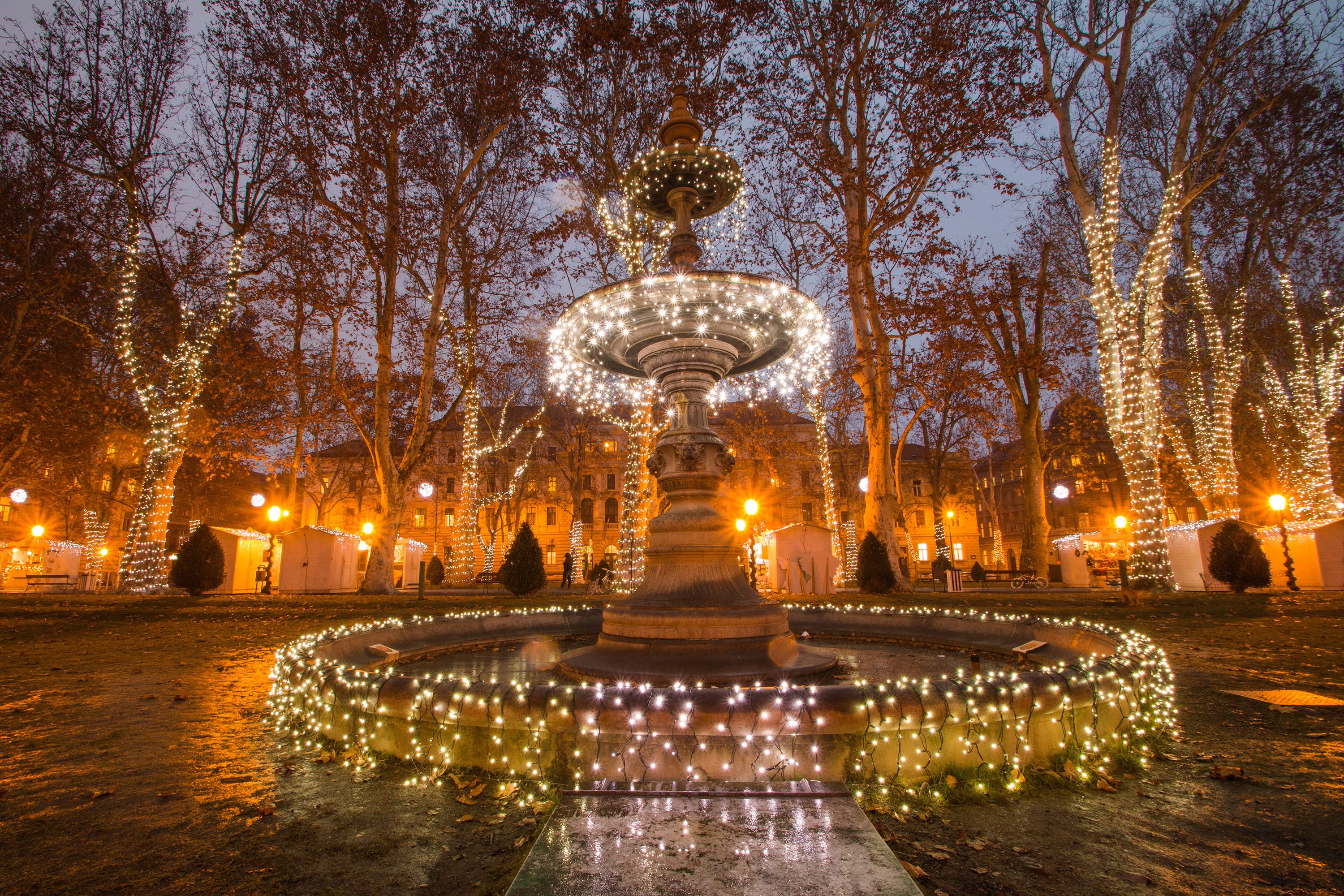 Illuminated fountain in Zrinjevac park, Zagreb, with Christmas market stalls in the background