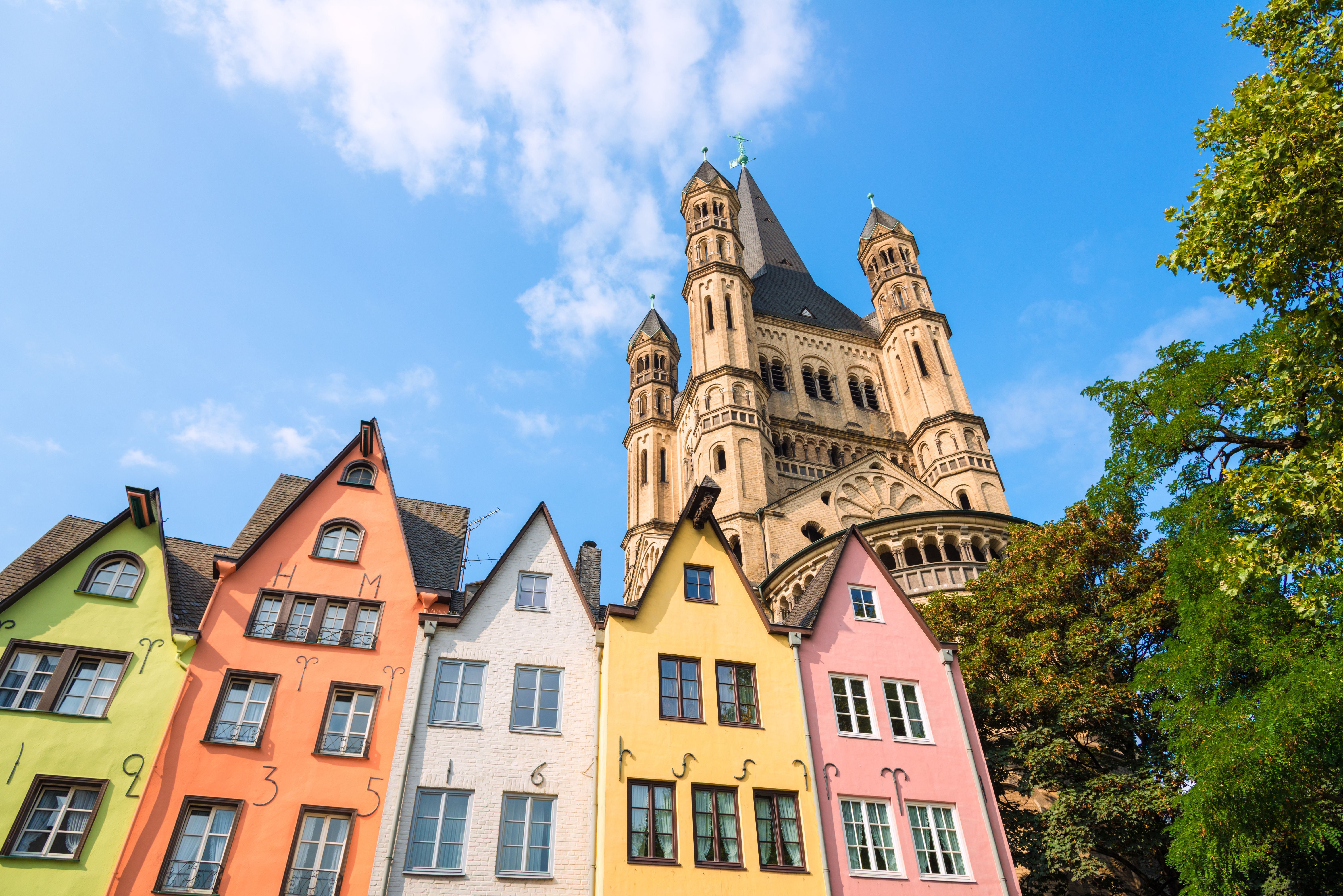 Looking up at pastel coloured houses and the tower of a church on a sunny day in Cologne