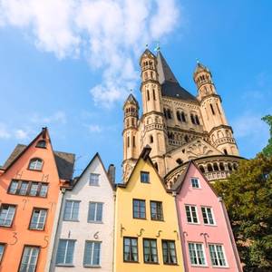 Looking up at pastel coloured houses and the tower of a church on a sunny day in Cologne