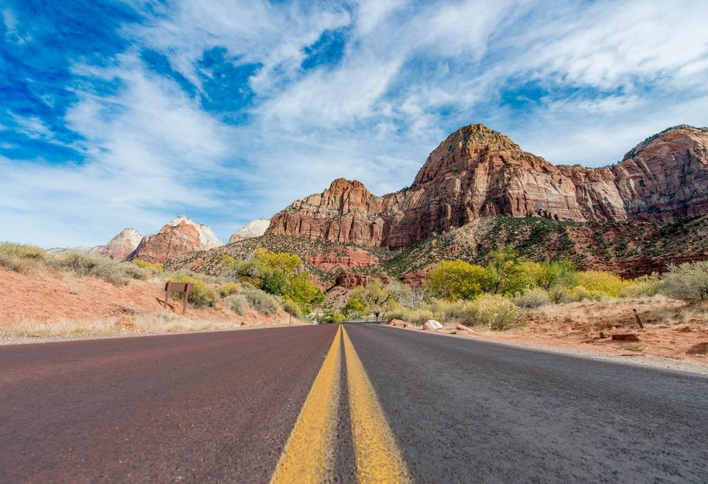 An empty road stretches towards the steep red cliffs of Zion National Park