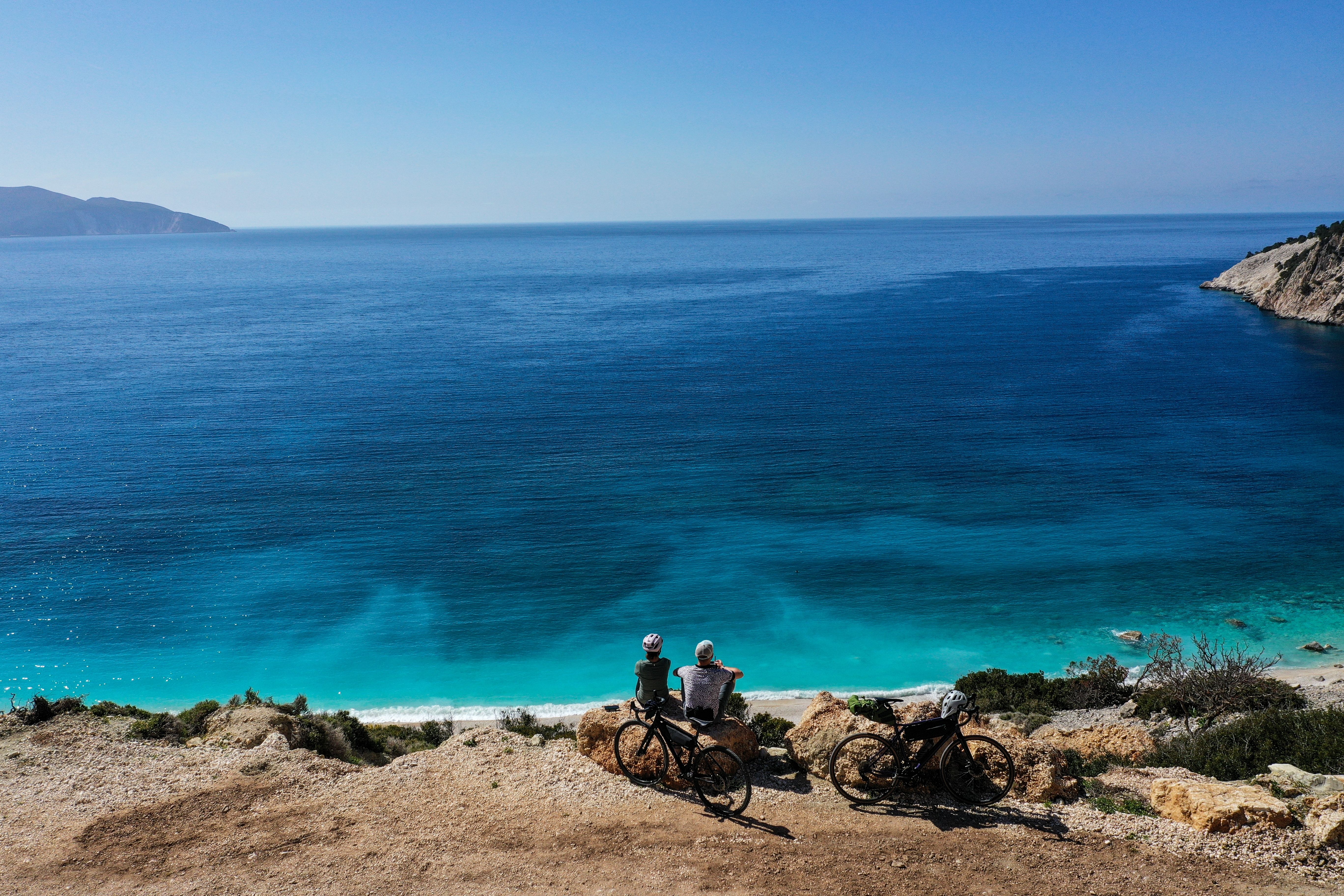 Two cyclists on a scenic winding road above famous Myrtos Beach on the island of Kefalonia, Greece