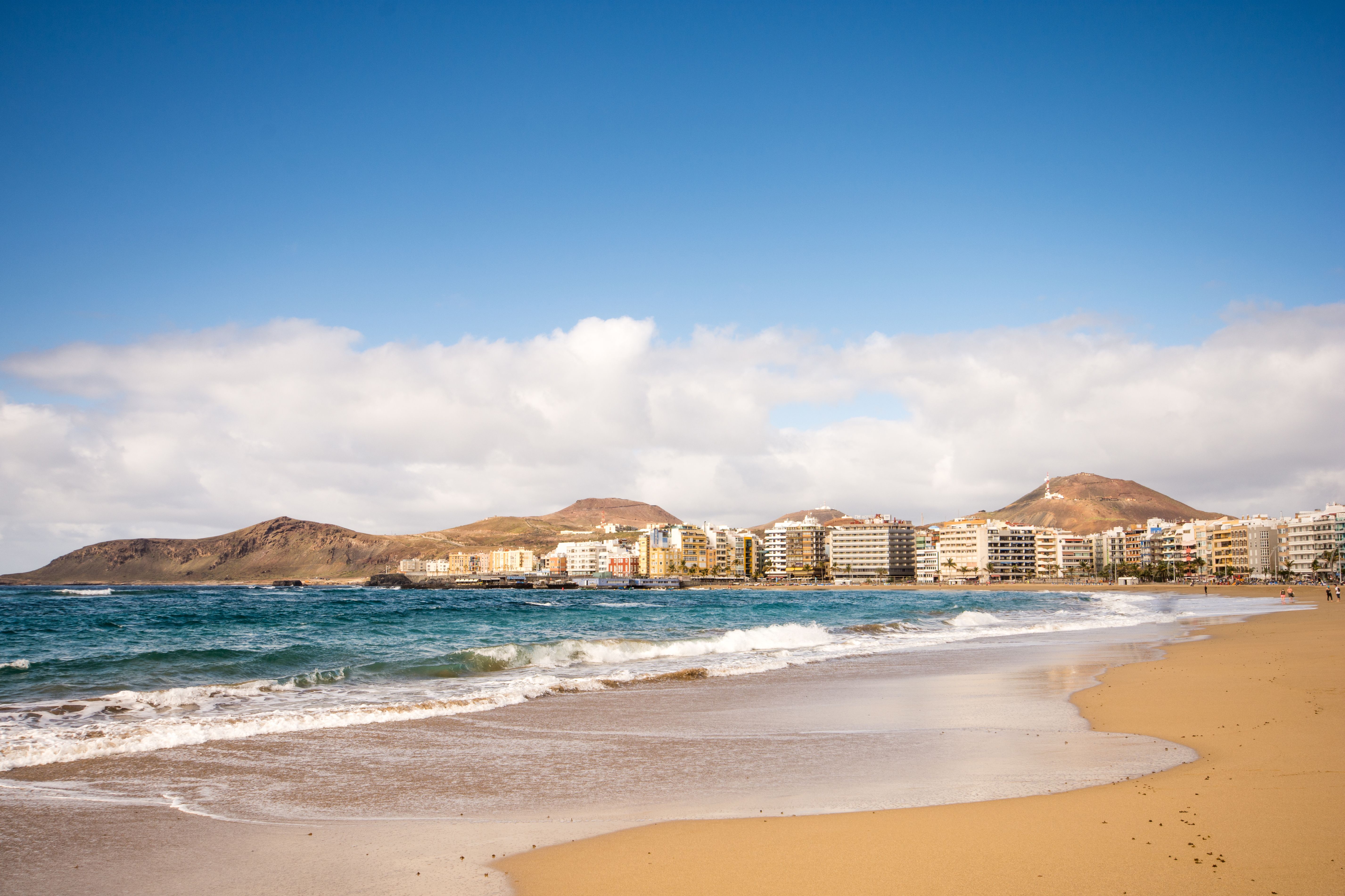 View of waves crashing on the golden sands of Las Canteras beach with the low-rise apartments of the city in the background