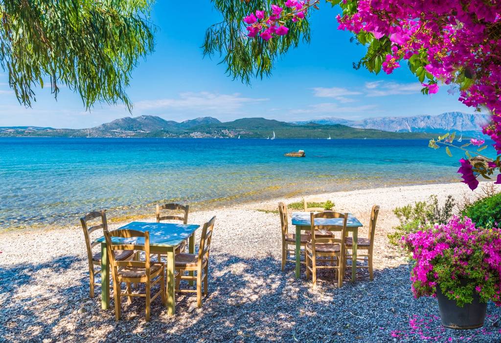 A view of the sea from Nikiana beach on the island of Lefkada, Greece, with tables and chairs arranged on the beach belonging to a taverna on a sunny day.