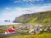 View of a white and red church overlooking a small town at the foot of dramatic cliffs with the sea stacks of Vik beach in background