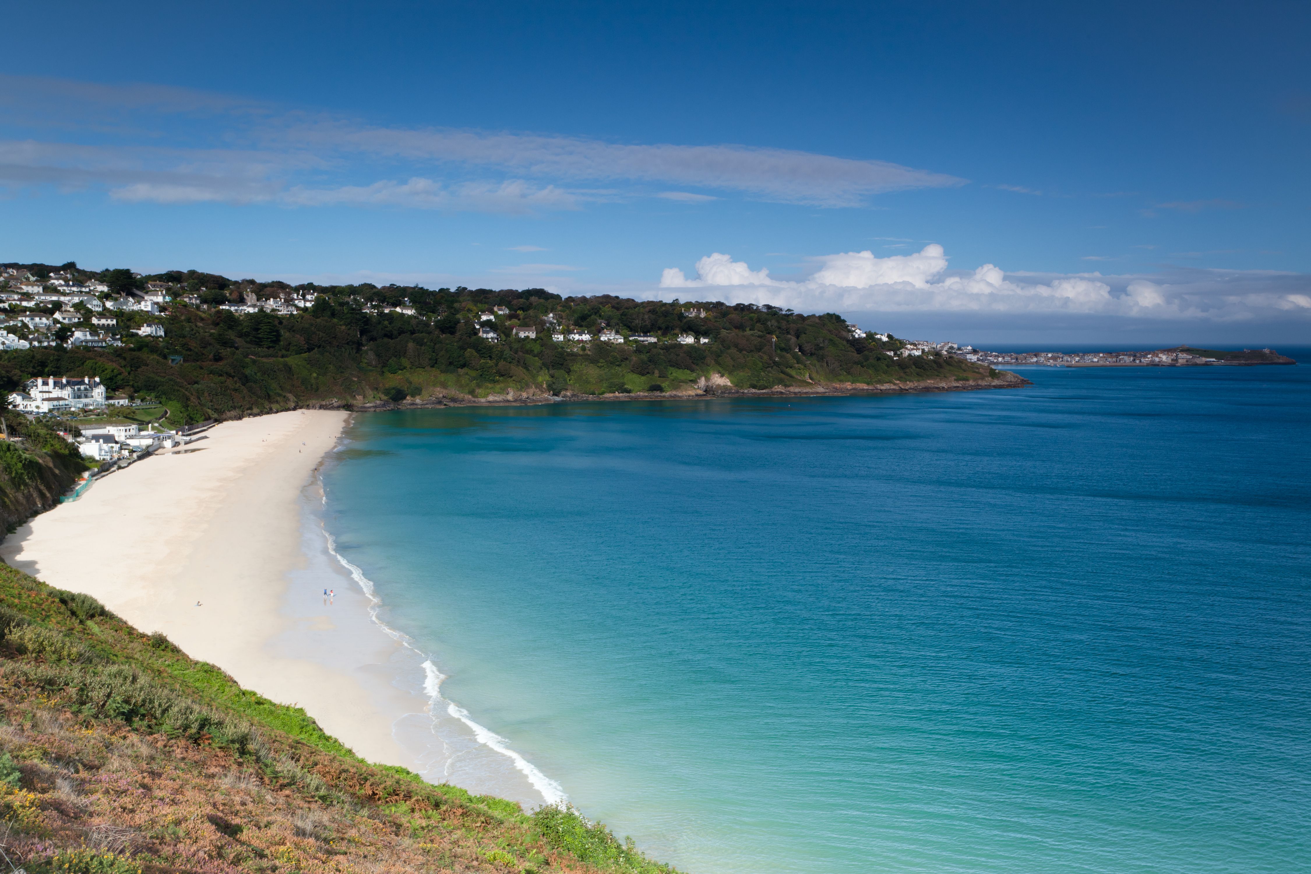 View of an empty light-gold beach with calm turquoise waters lapping the shore.