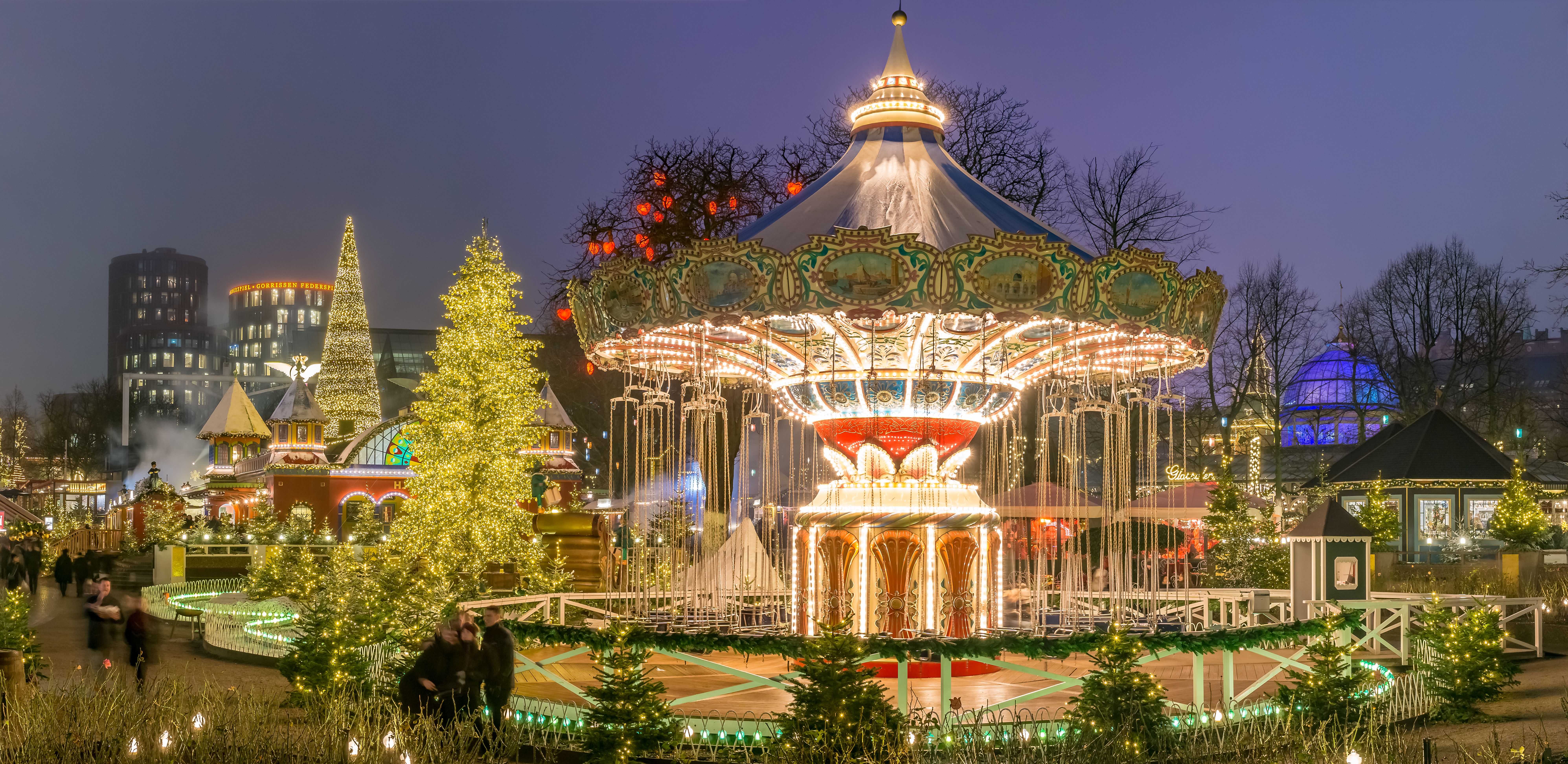 A view of the Christmas market in Tivoli Gardens, Copenhagen with brightly lit fairground rides and Christmas trees