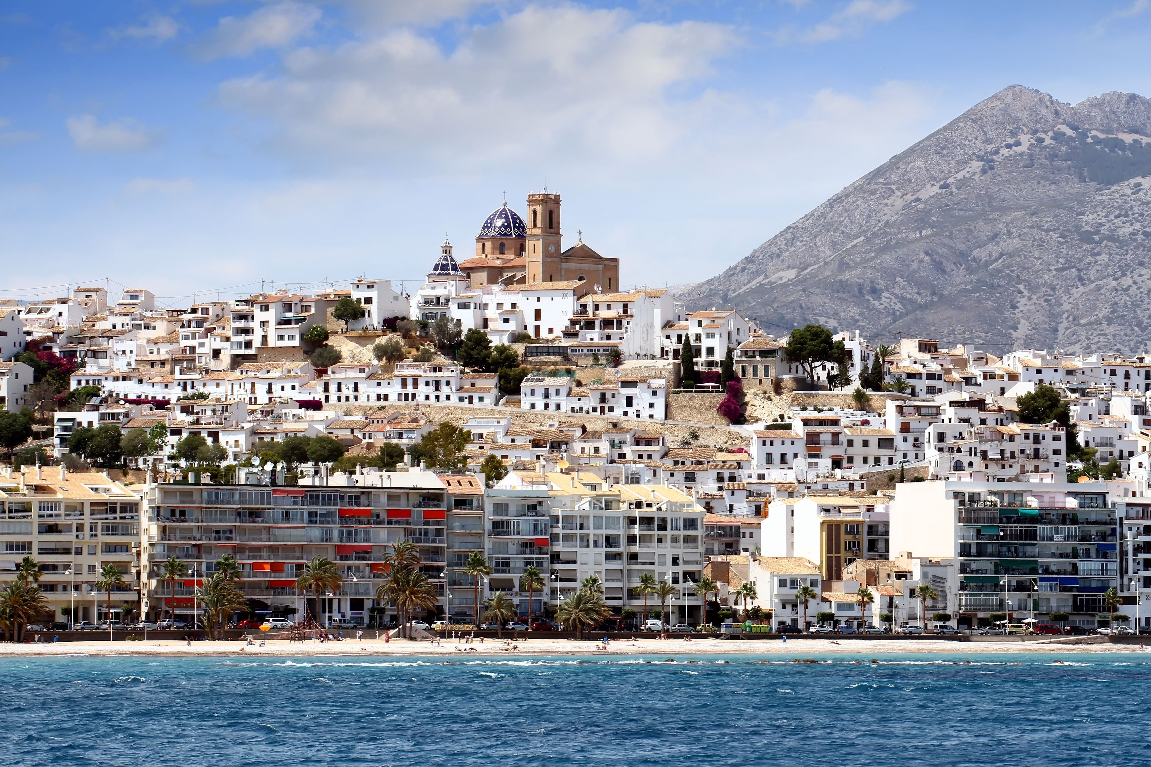 View of the whitewashed building of a seaside town with a blue-domed church overlooking it all.