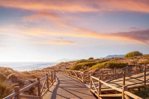 A view of a wooden walkway across the Artola Dunes and beach in Cabopino Natural Park in Marbella, Spain at sunset