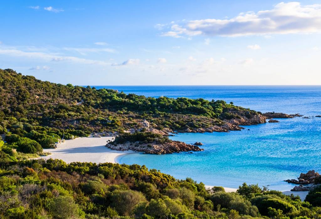 A sunny day on a small sandy cove surrounded by lush vegetation and lapped by clear Mediterranean waters 