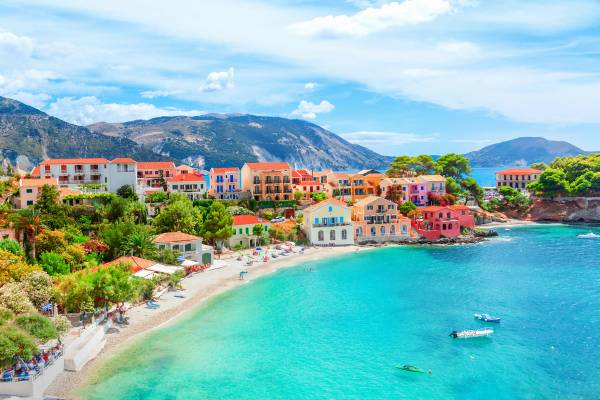 A picture of the colour village of Assos in Kefalonia, with traditional houses along the bay showing a sandy beach and clear blue water