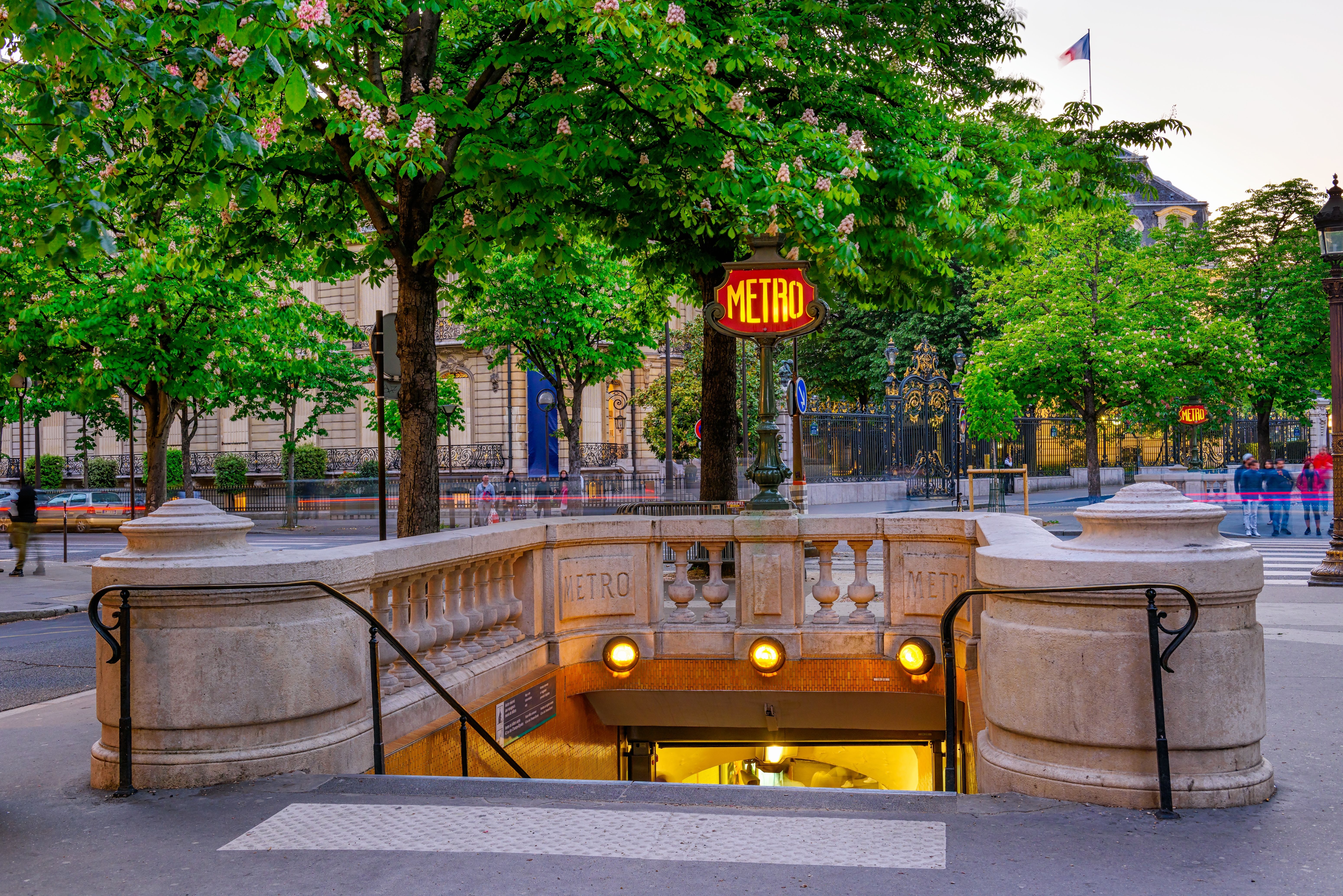 A view of the entrance to a metro station in Paris with green trees in the background
