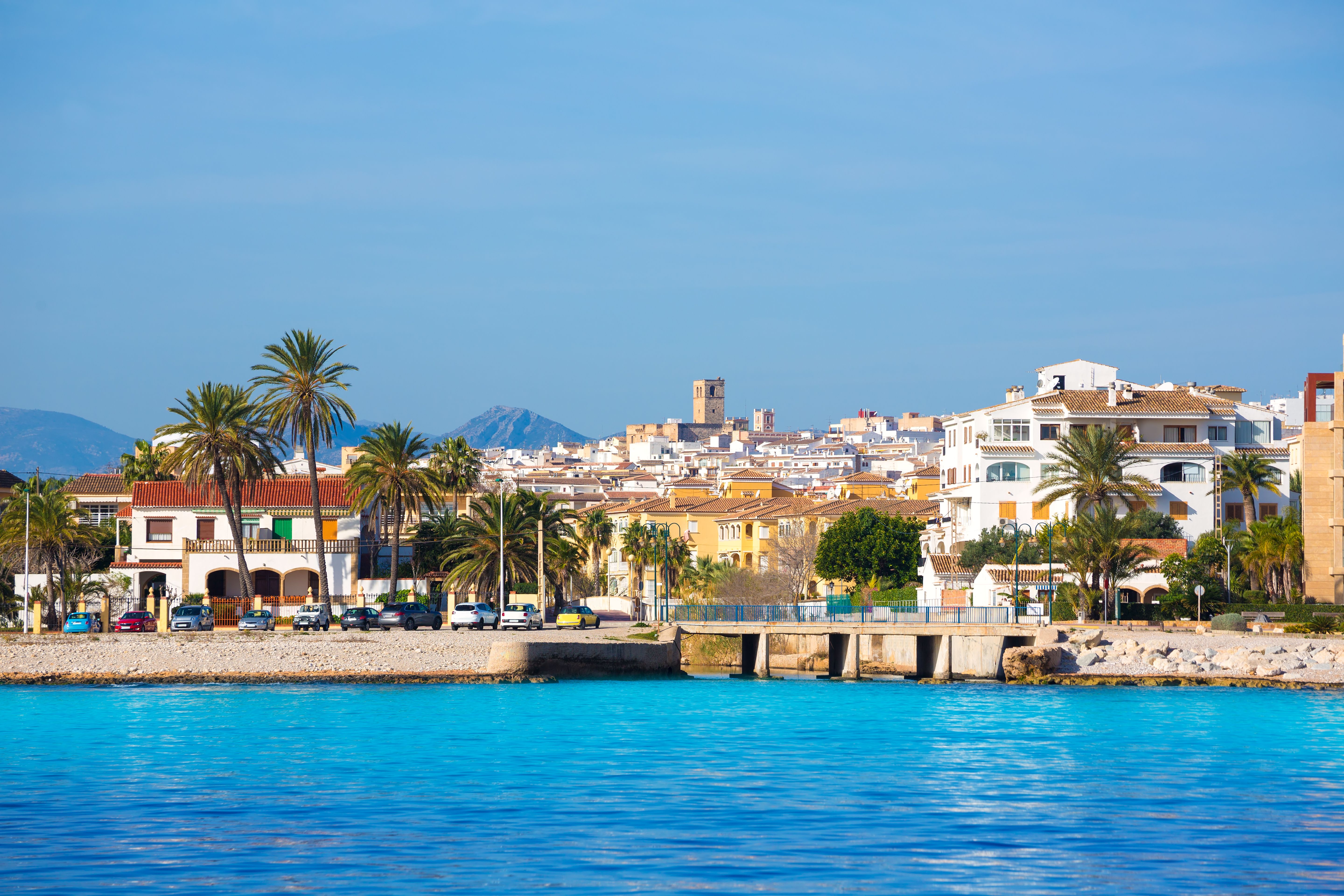 View across the water to the skyline of a whitewashed Spanish town on a sunny day.
