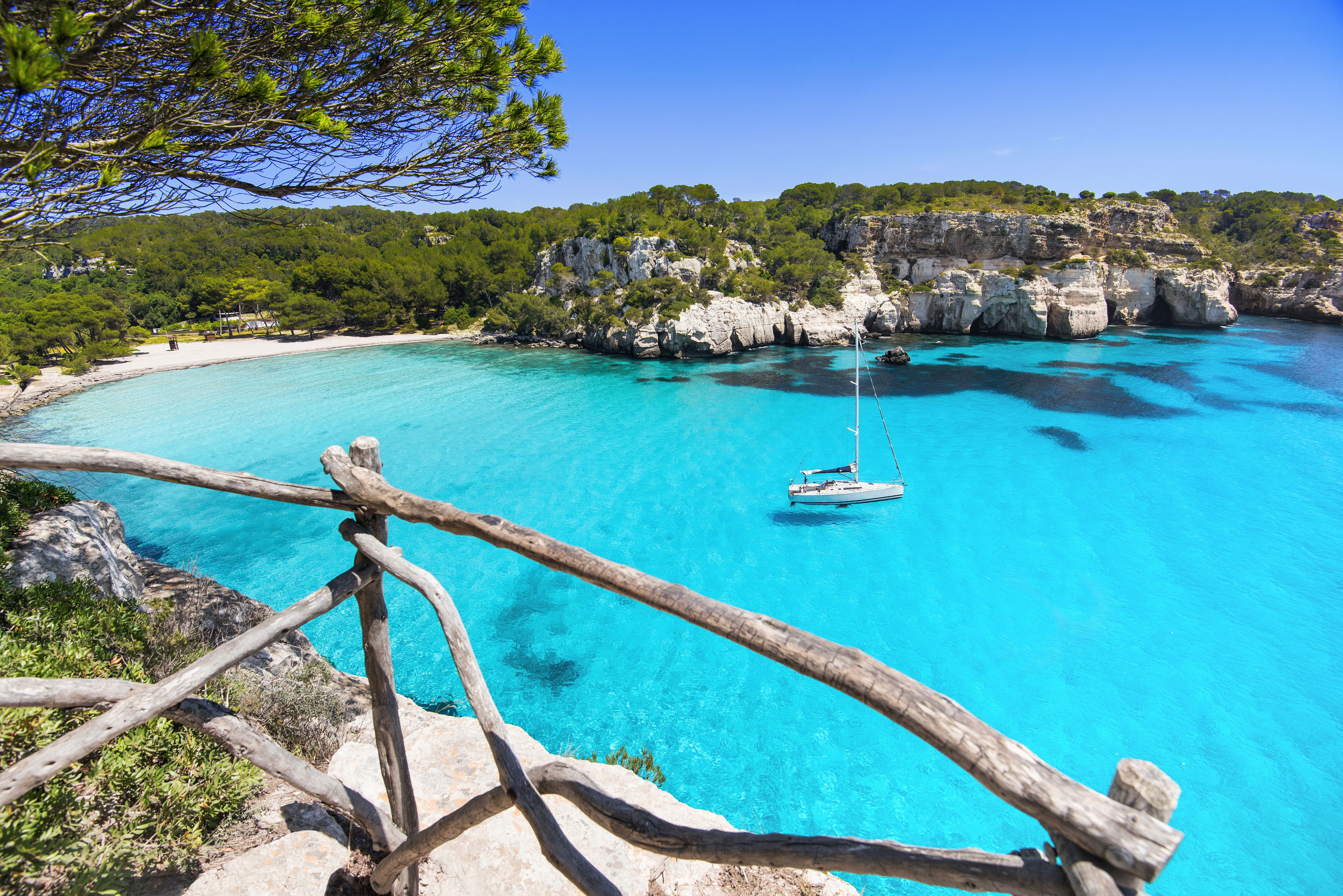View of a solo sailing boat floating on the incredibly clear waters of Cala Macarella