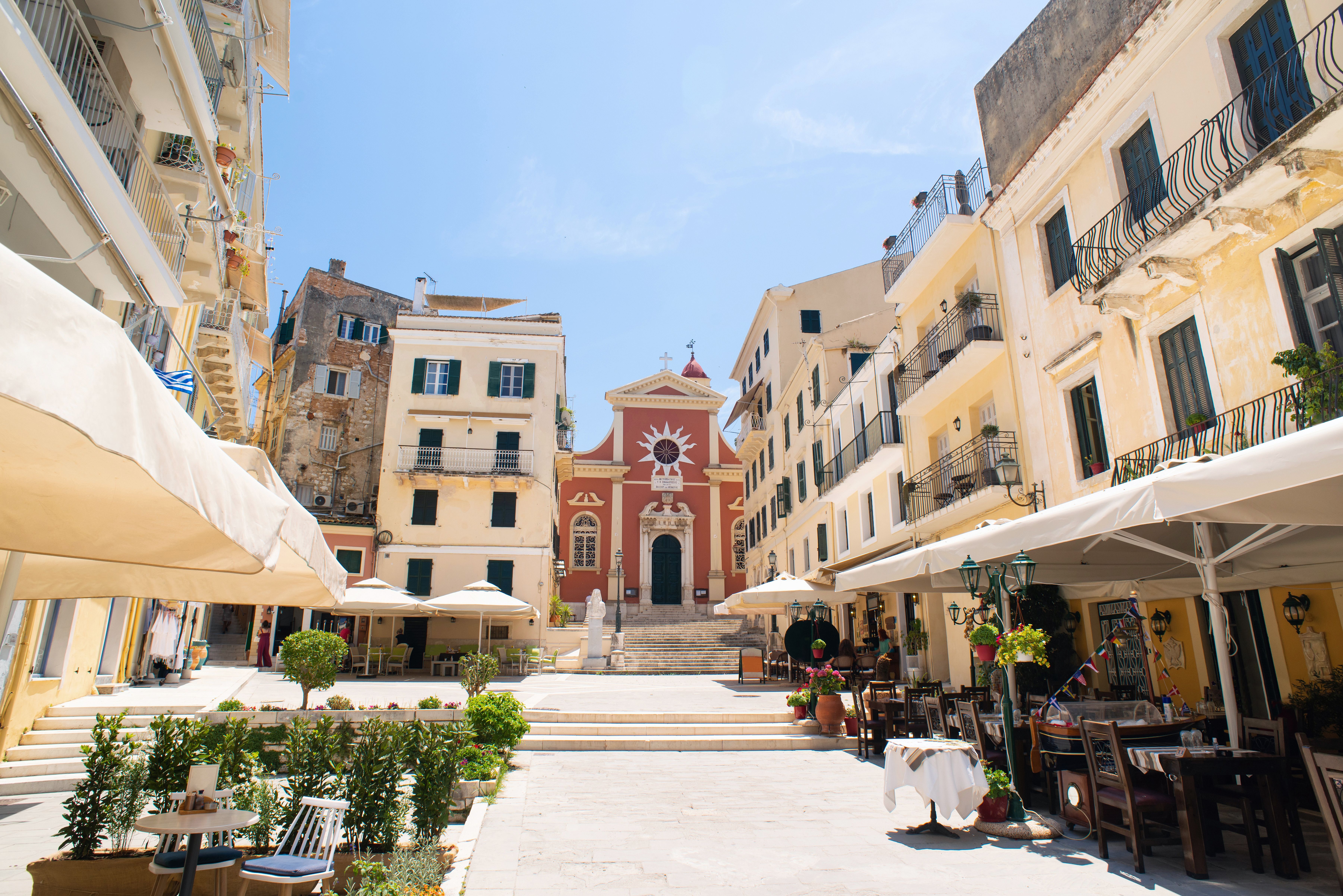 View across an old town square lined with cafes with outdoor seating and a red church in the distance