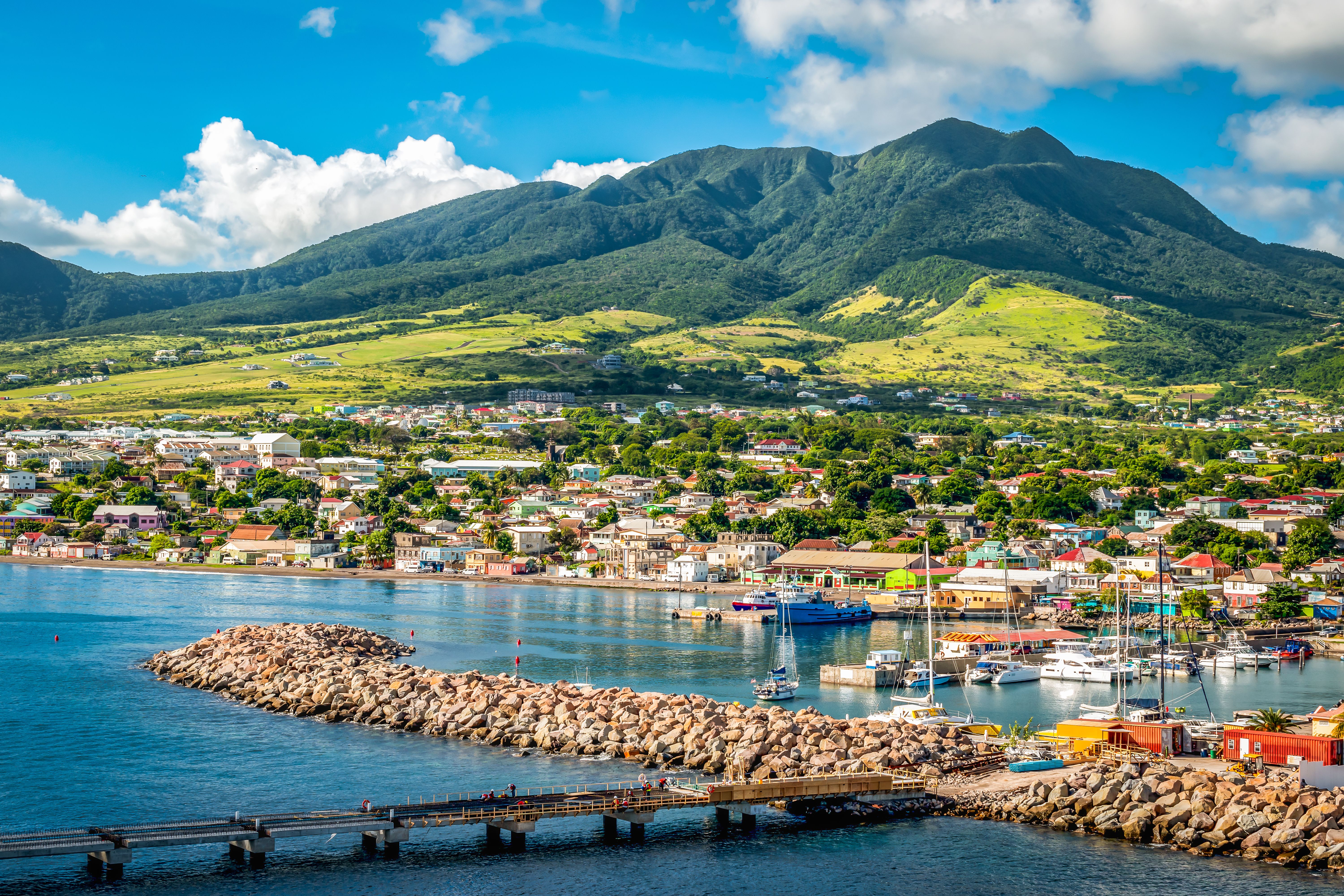 A view of St Kitts Island in the Caribbean with a rock spit bank harbouring colourful fishing boats and lush green mountains in the background