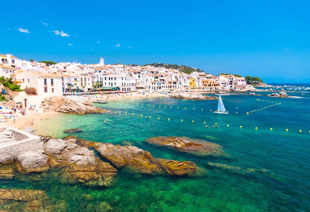 A view of the beach town of Calella de Palafrugell, Girona with white washed buildings lining the beachfront and aqua-green sea