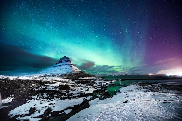 A magical snowy view of the colourful Northern lights in Mount Kirkjufell Iceland with green and pink lights at night time
