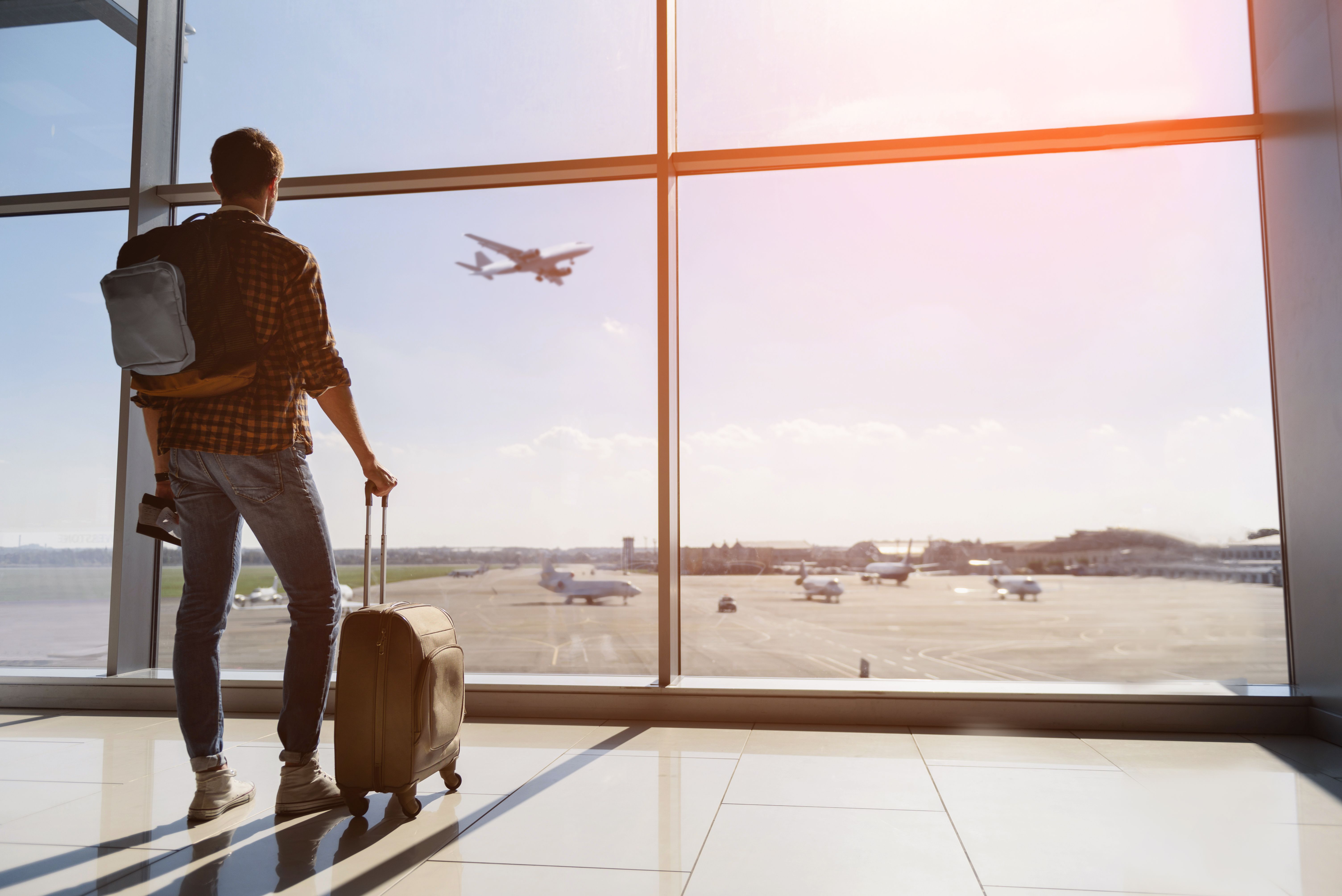 A picture of a young man watching a plane taking off from inside of an airport