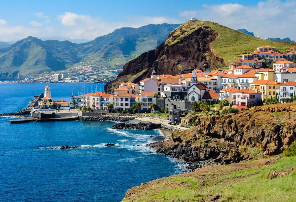View of a coastal town with whitewashed houses with red roofs surrounded by green mountains