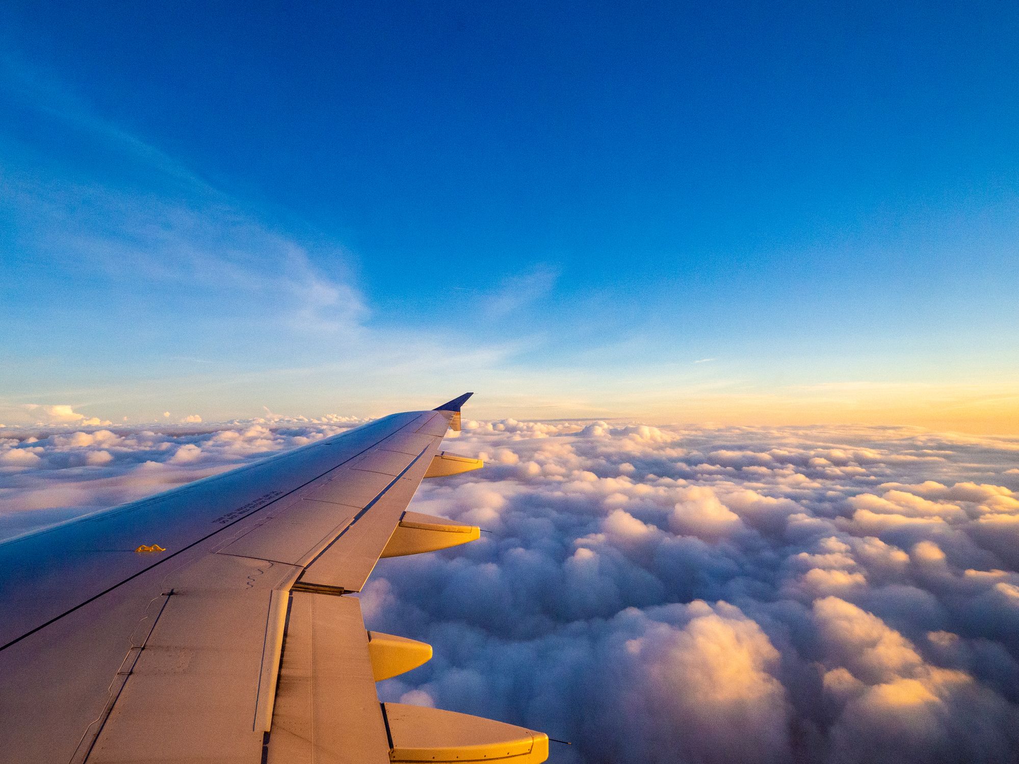 A view from the right side window of an plane showing the aircraft wing during a sunrise over the clouds