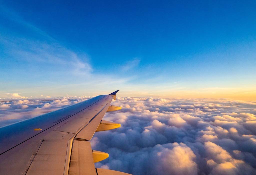 A view from the right side window of an plane showing the aircraft wing during a sunrise over the clouds