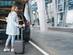 A woman stands at the back of a vehicle holding a boarding ticket and a trolley suitcase.