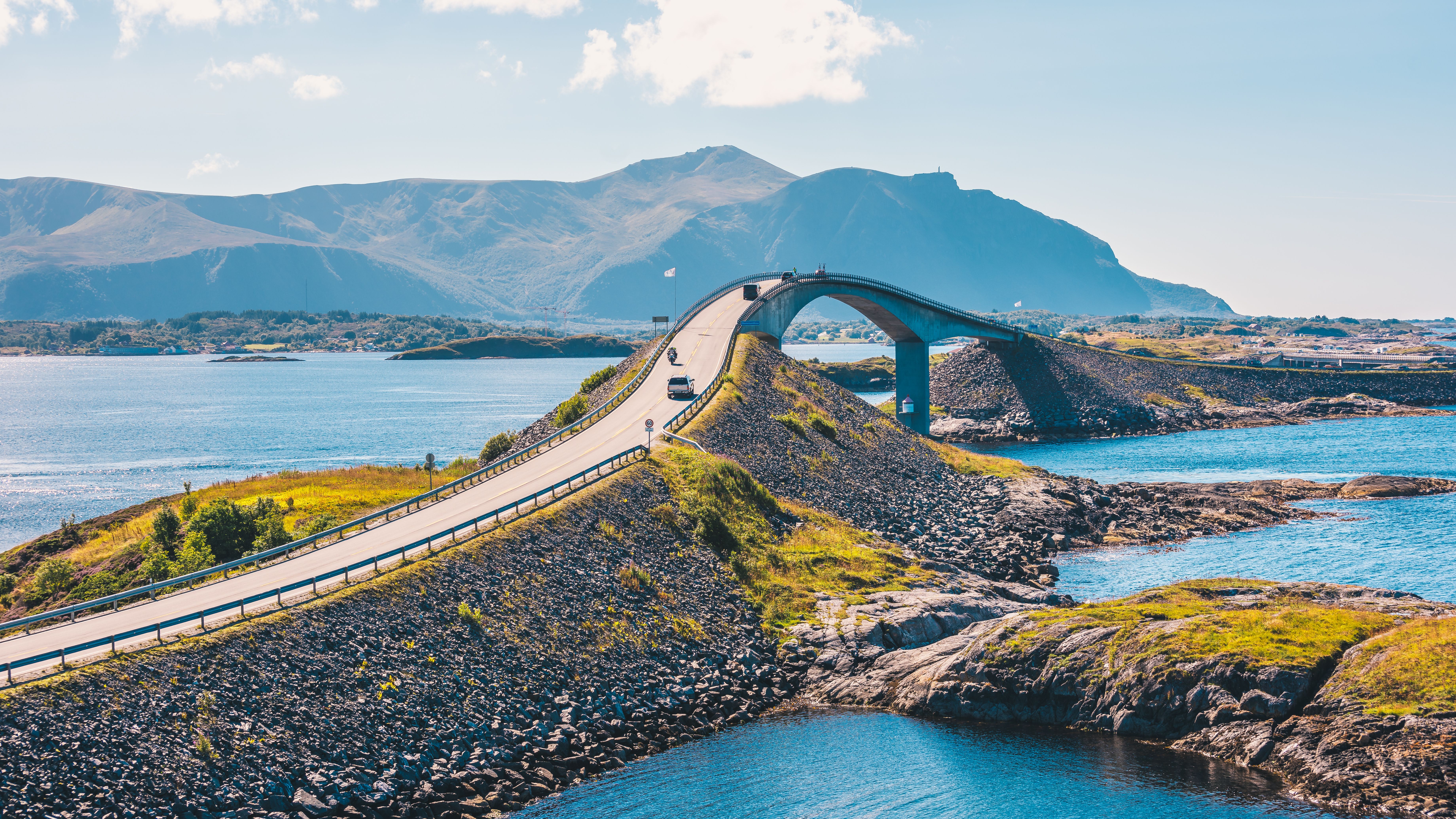 View of a steeply arched bridge connecting two islands over the Atlantic with mountains in the background in Norway