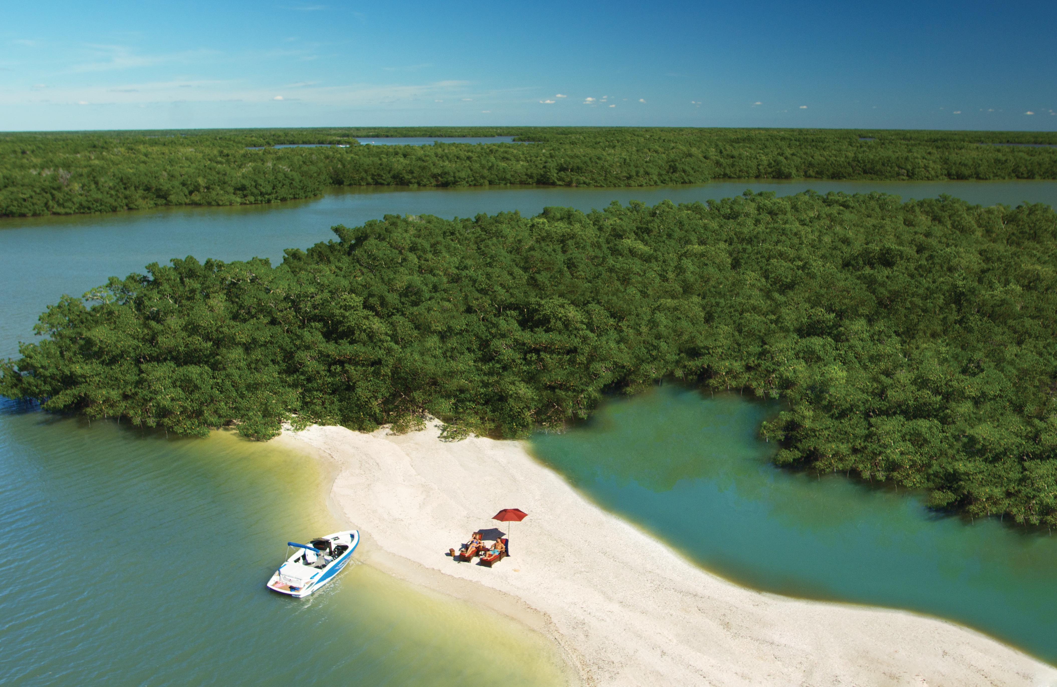 View of a boat anchored by a strip of pristine sand where two people are sunbathing.