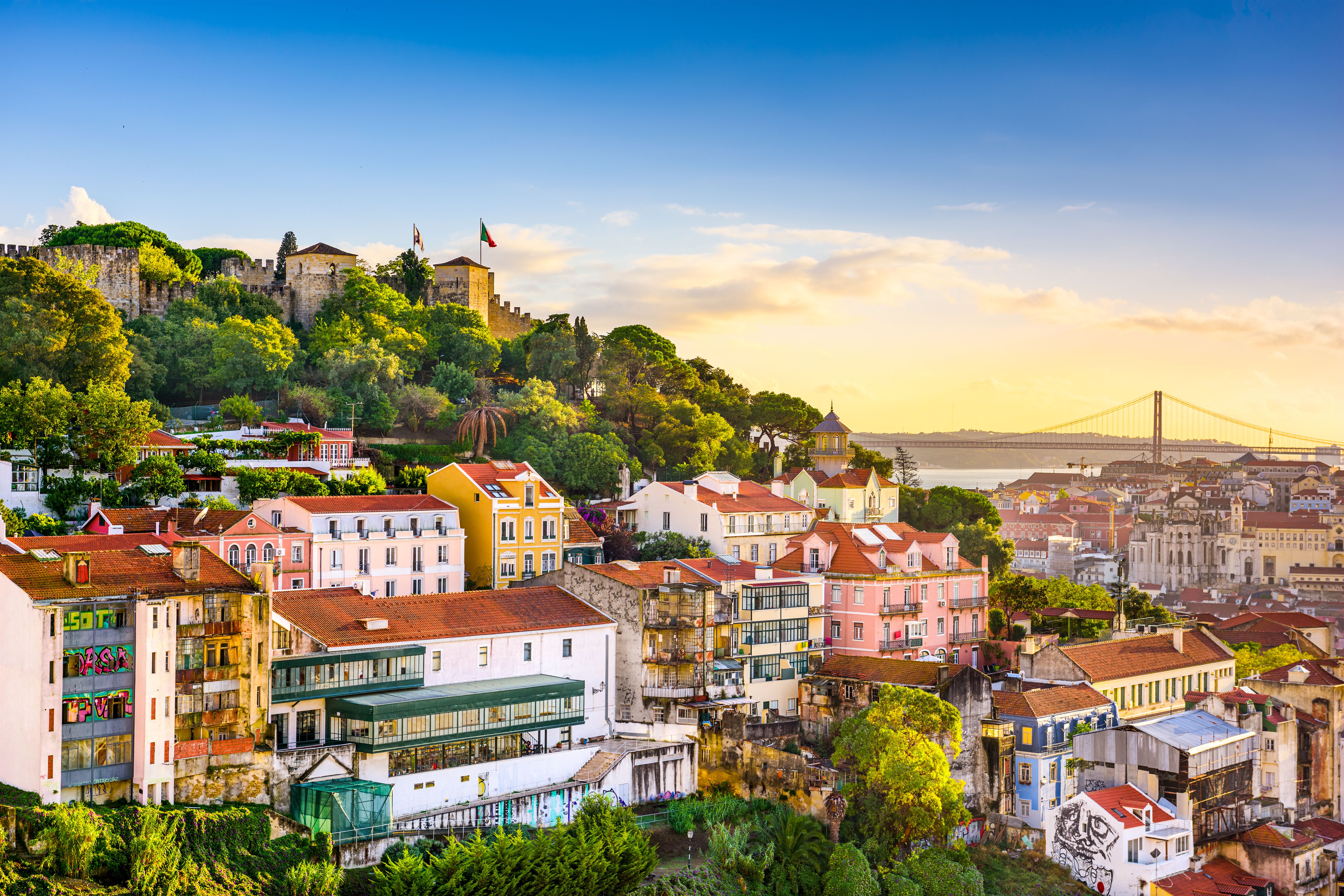 A view showing the skyline of the Lisbon's old town in Portugal, including the Sao Jorge Castle atop of the hill, and the Ponte 25 de Abril bridge in the horizon.