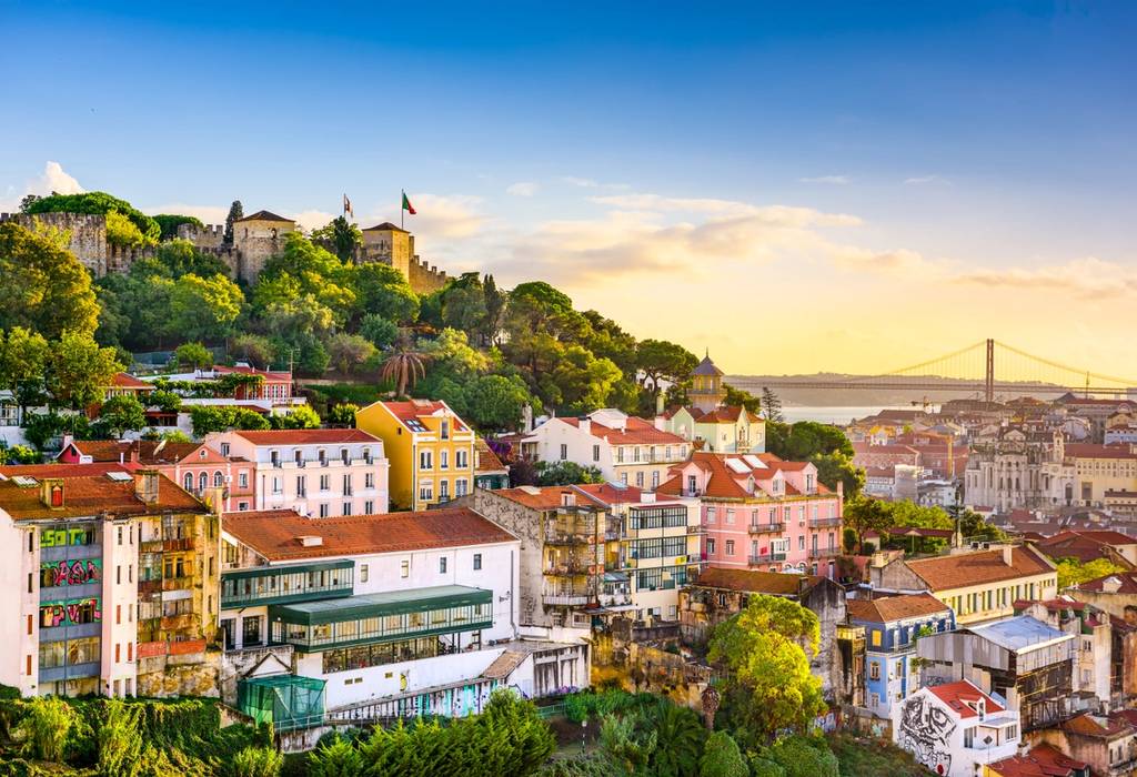 A view showing the skyline of the Lisbon's old town in Portugal, including the Sao Jorge Castle atop of the hill, and the Ponte 25 de Abril bridge in the horizon.