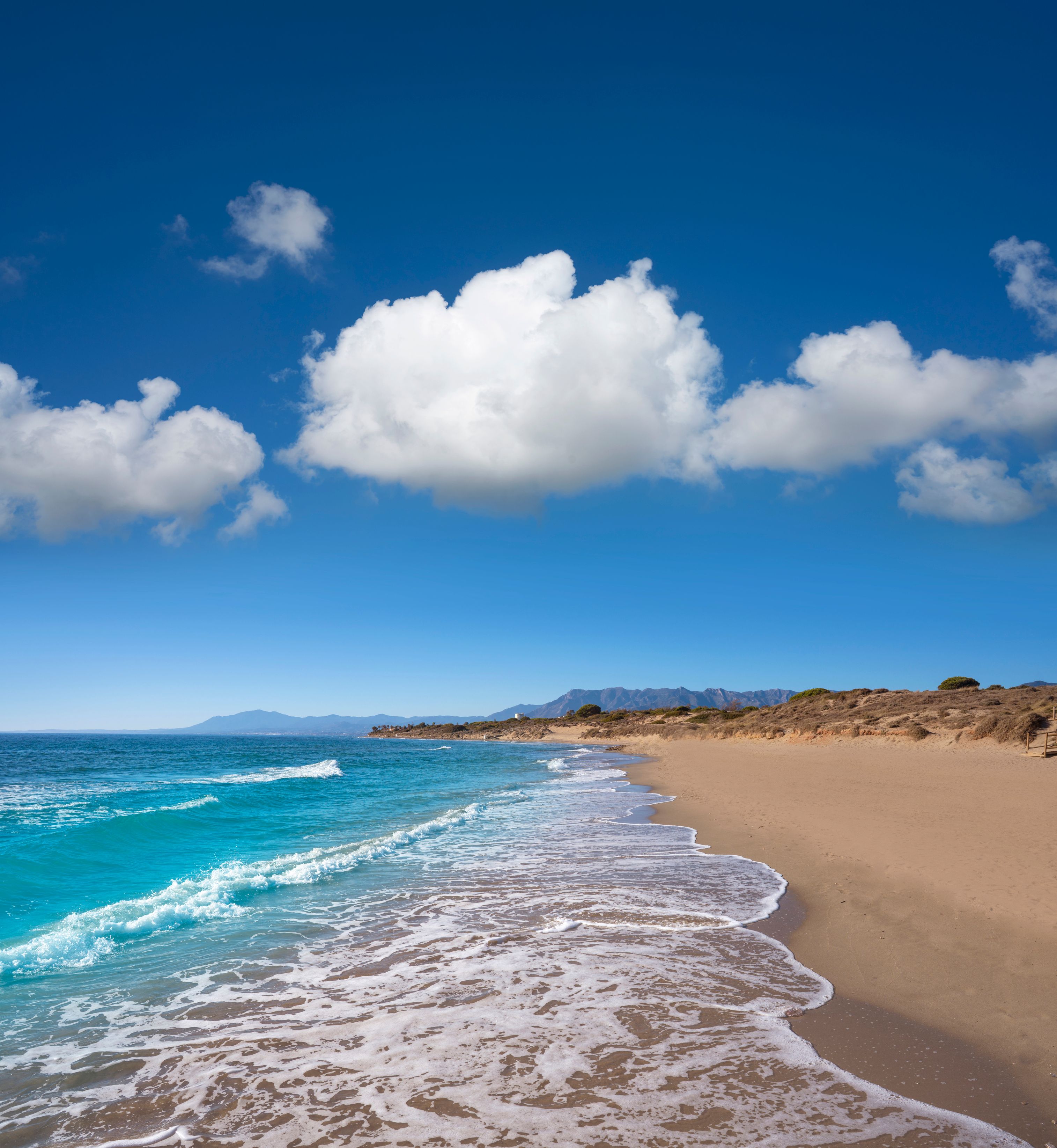 Brilliant blue waves lapping the empty, golden shores of Artola Beach