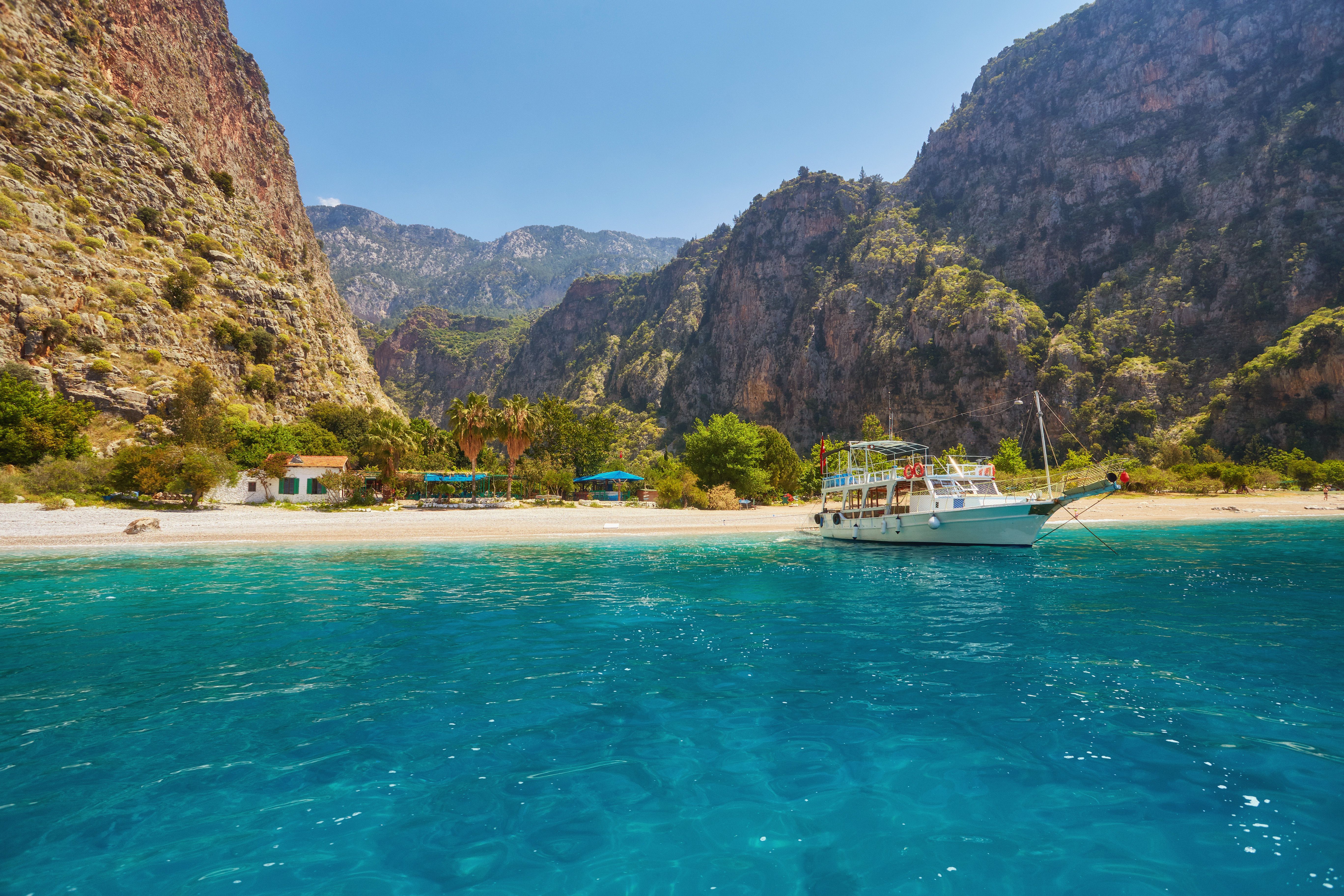 View across turquoise waters towards a sandy beach backed by dramatic, vegetation-covered cliffs