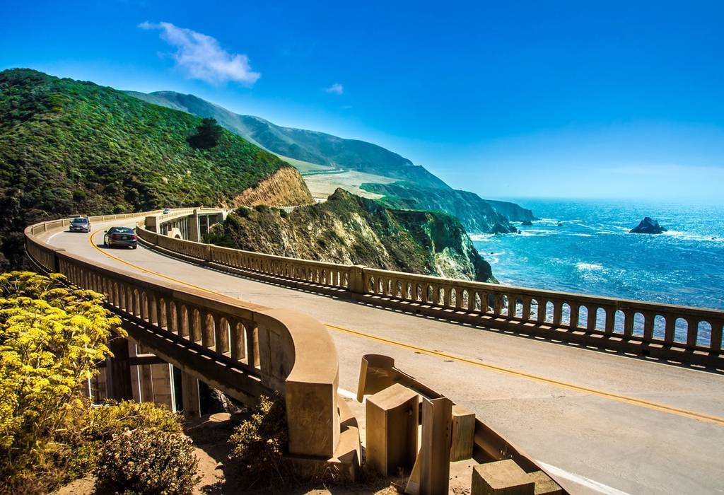 A view of Bixby Creek Bridge on the Highway #1 in California, USA with green cliffs to the right and ocean views to the left.