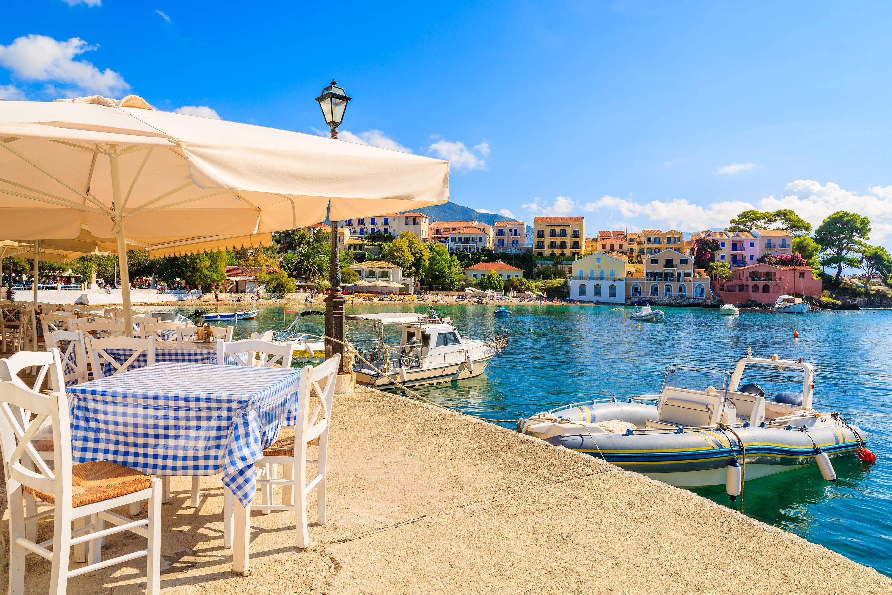 View of a cafe with shaded tables overlooking a bay with boats in Kefalonia