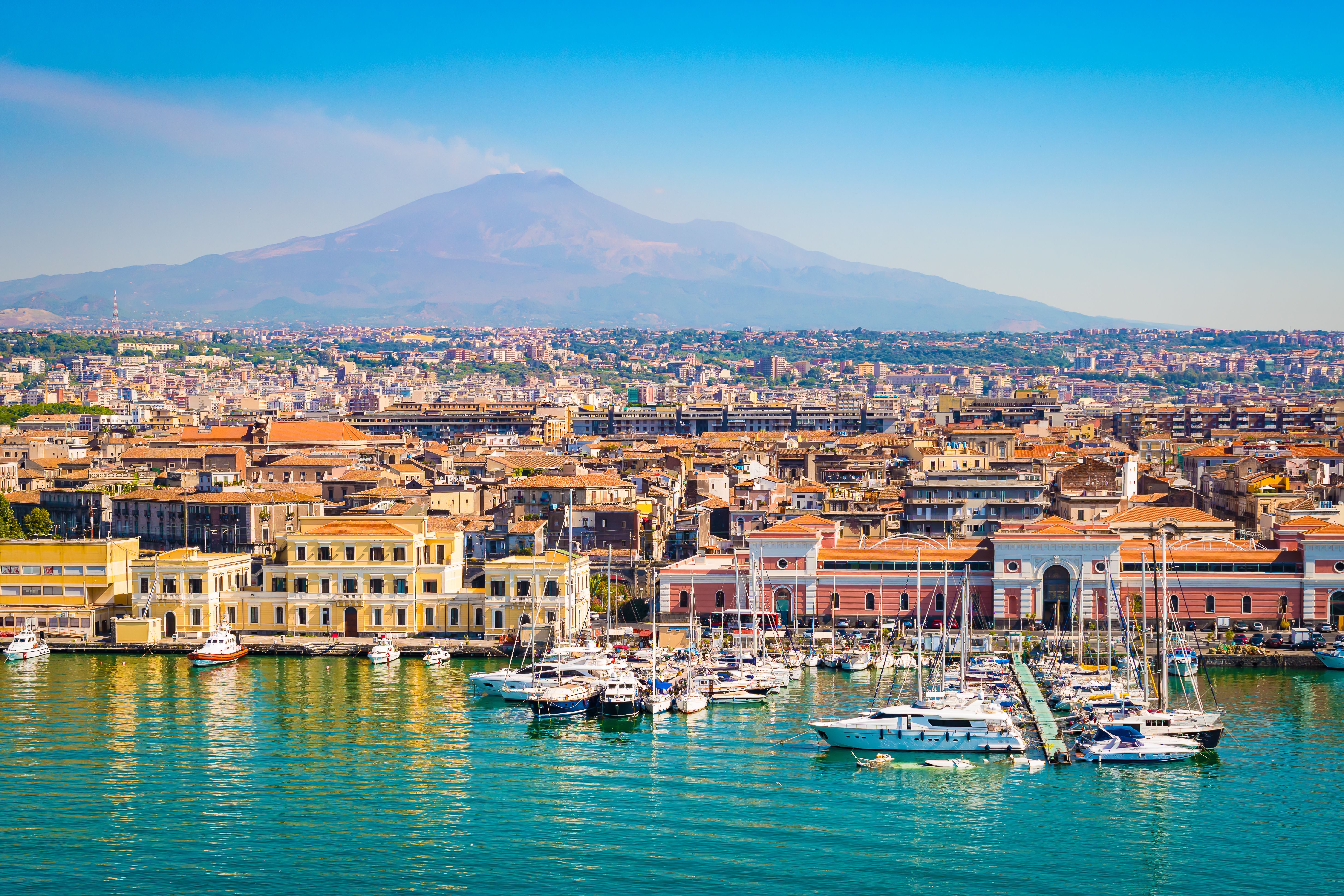 A view of the Catania's colourful harbourfront with boats and yachts docked in the marina and Mount Etna in the background Sicily, Italy