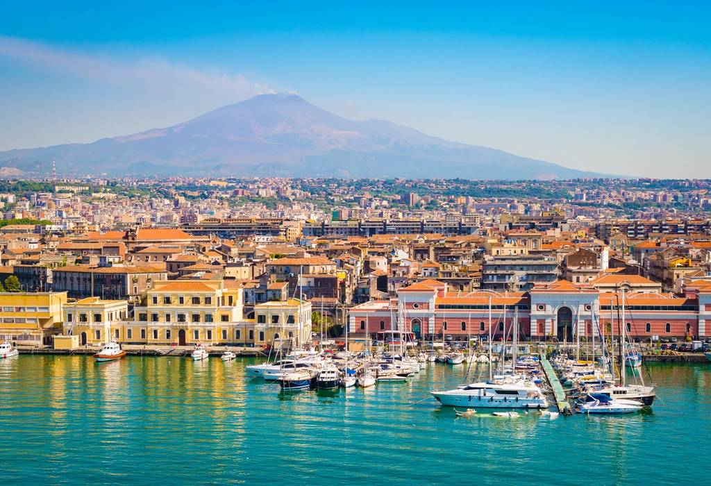 A view of the Catania's colourful harbourfront with boats and yachts docked in the marina and Mount Etna in the background Sicily, Italy