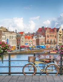 View of a canal in Amsterdam with a bike attached to a guard rail topped with pink and white flowers